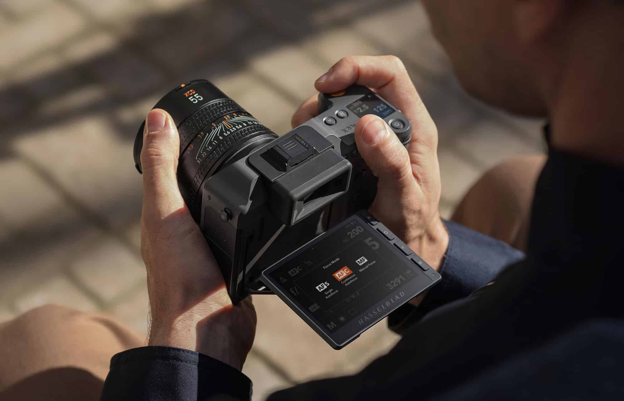 Photographer holding the X2D II 100C outdoors with its rear screen tilted upward.
