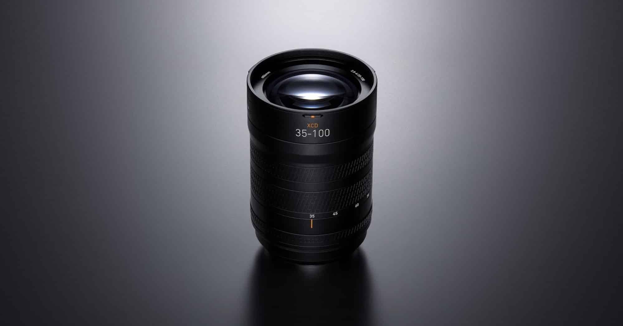 The 35-100E zoom standing alone in a pool of light on a dark reflective surface.