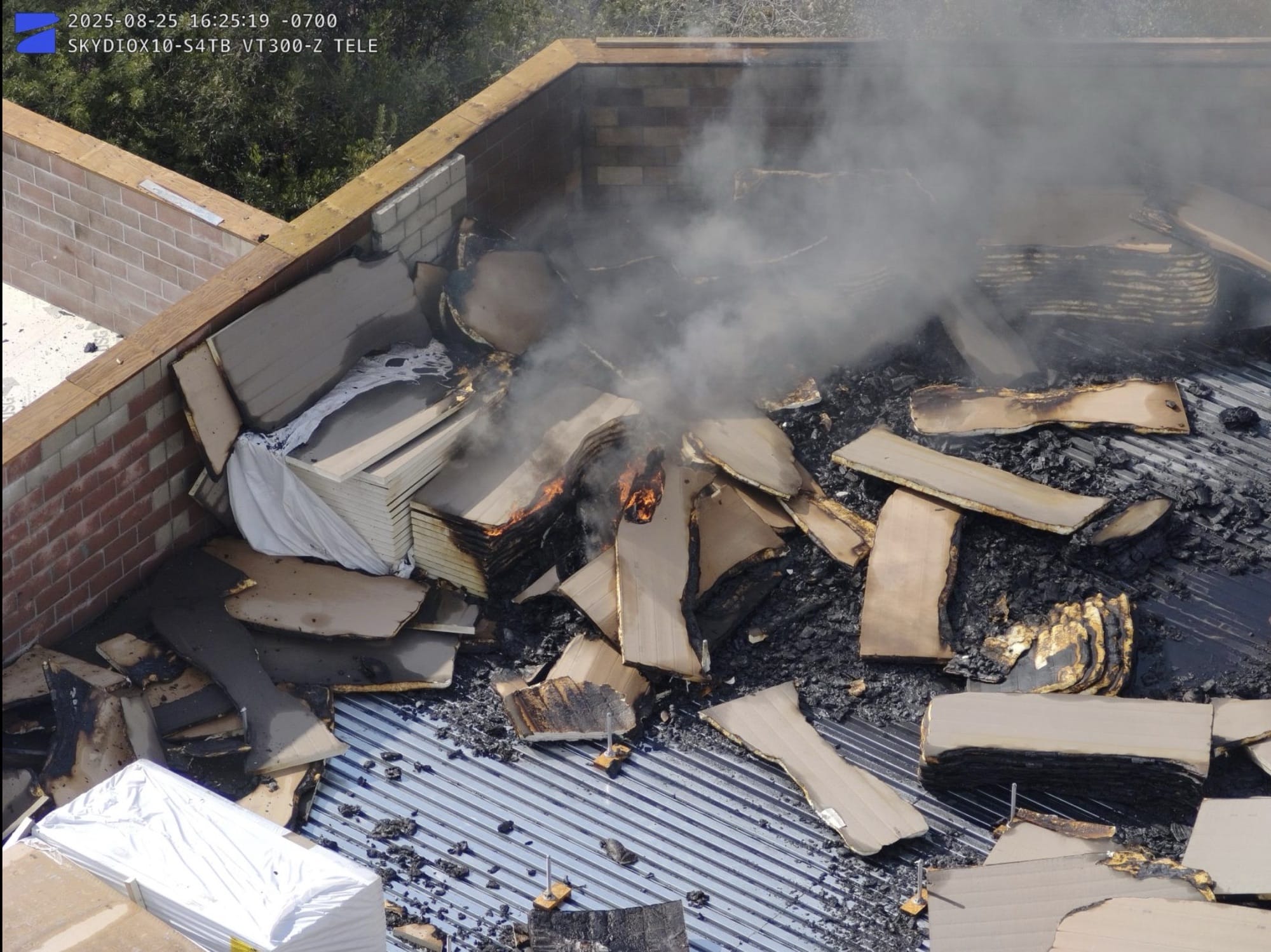 Timestamped drone footage of smoldering construction debris on a commercial rooftop.