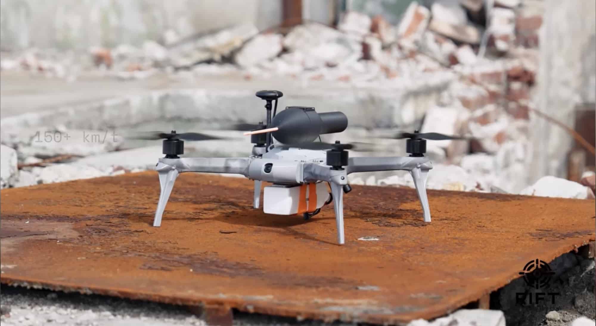 Quadcopter perched on a rusted steel plate in front of a rubble-strewn building.
