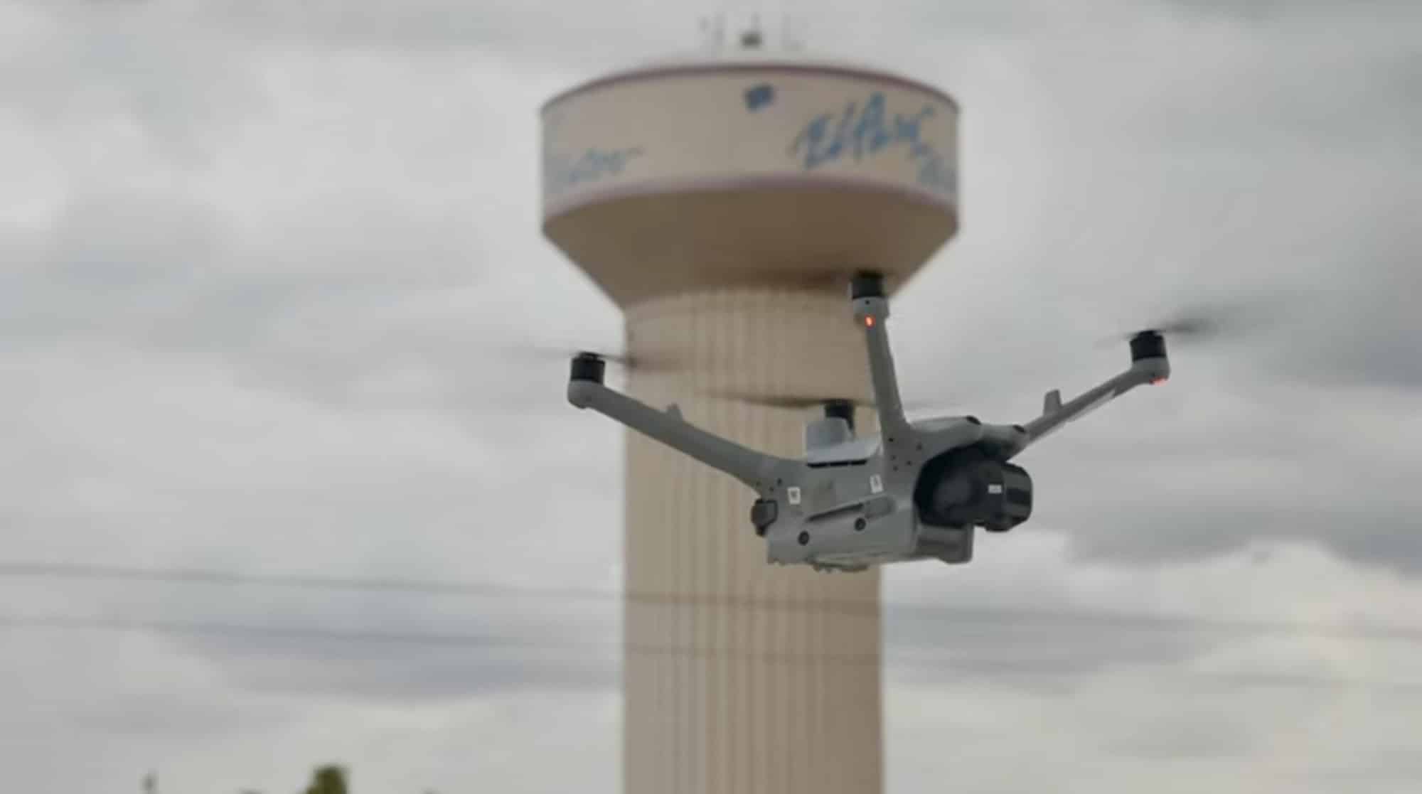 Quadcopter flying past a tan El Paso water tower under gray skies.
