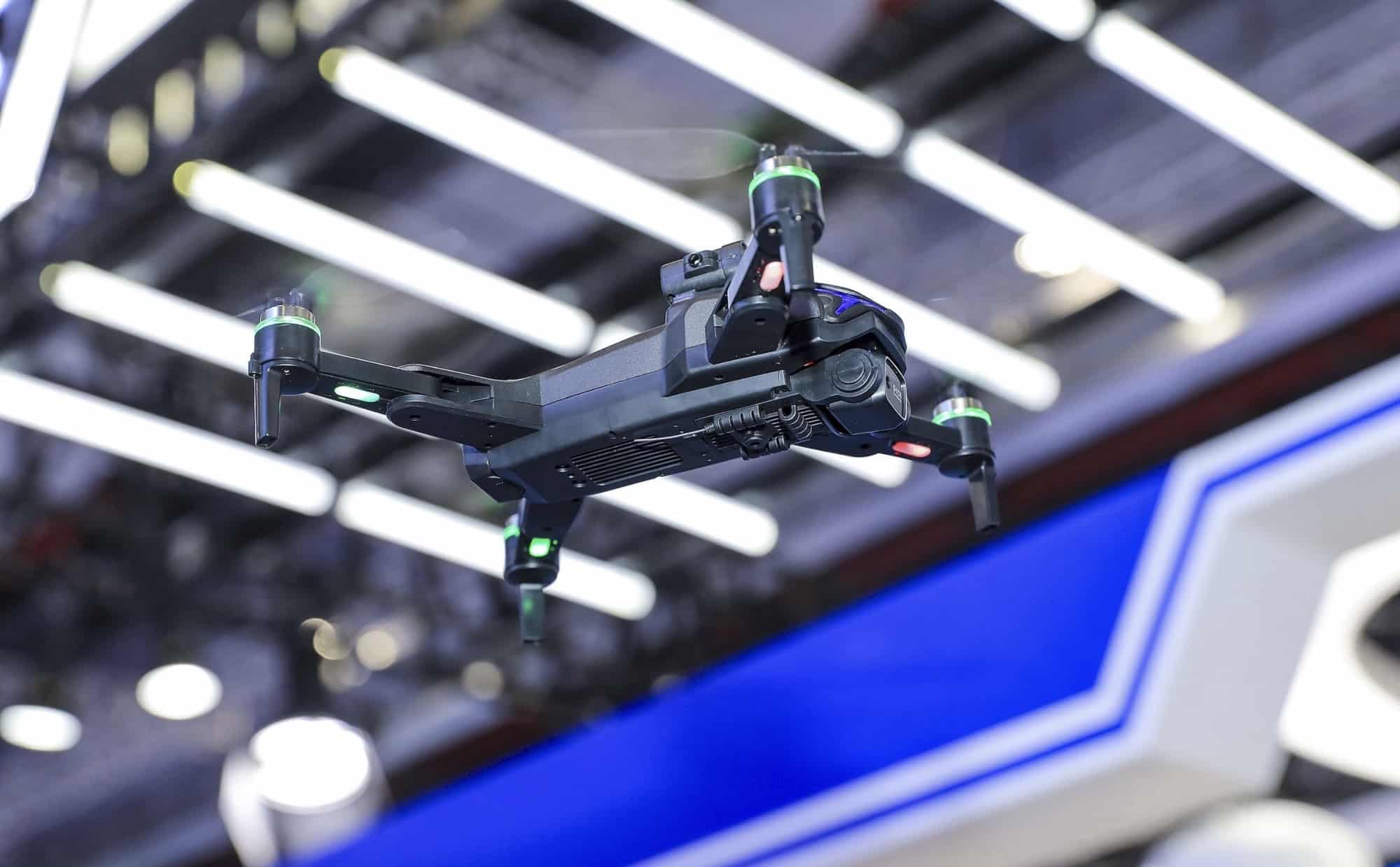 Black quadcopter displayed above a booth under bright exhibition lighting.