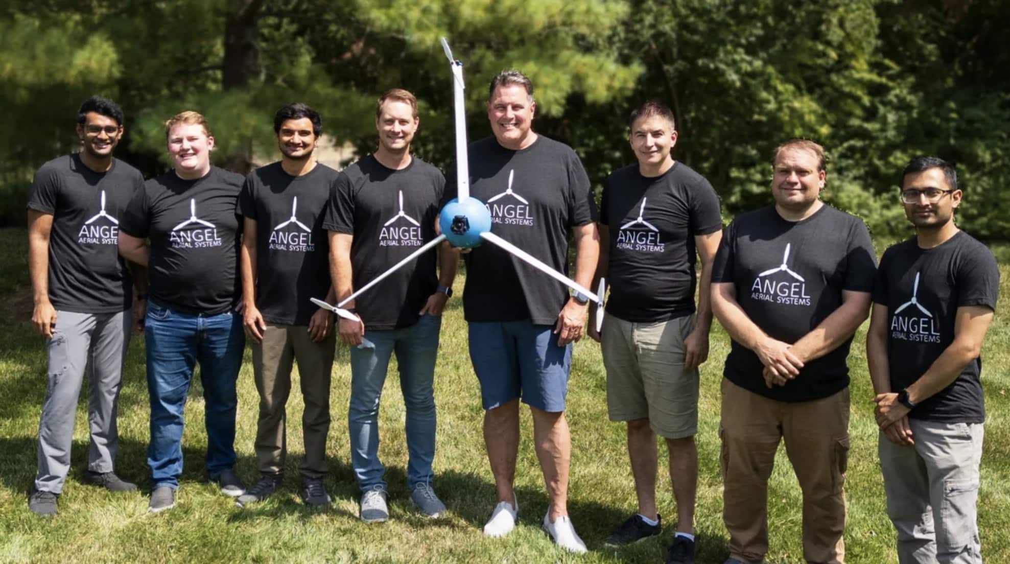 The Angel Aerial team poses outdoors holding their white Trio Scout tricopter.