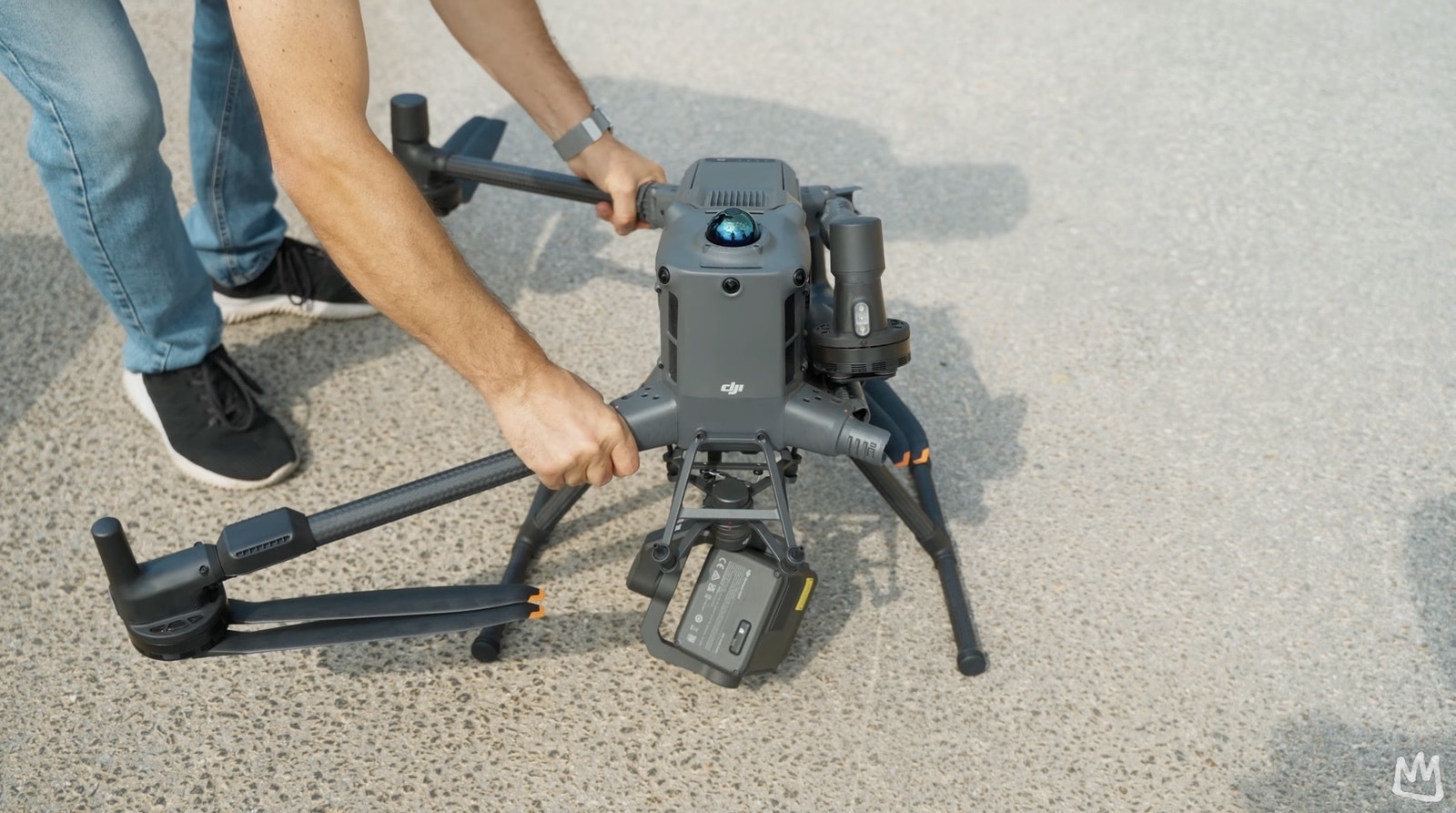 Operator lifts the folded Matrice 400 by its arms on a paved apron.