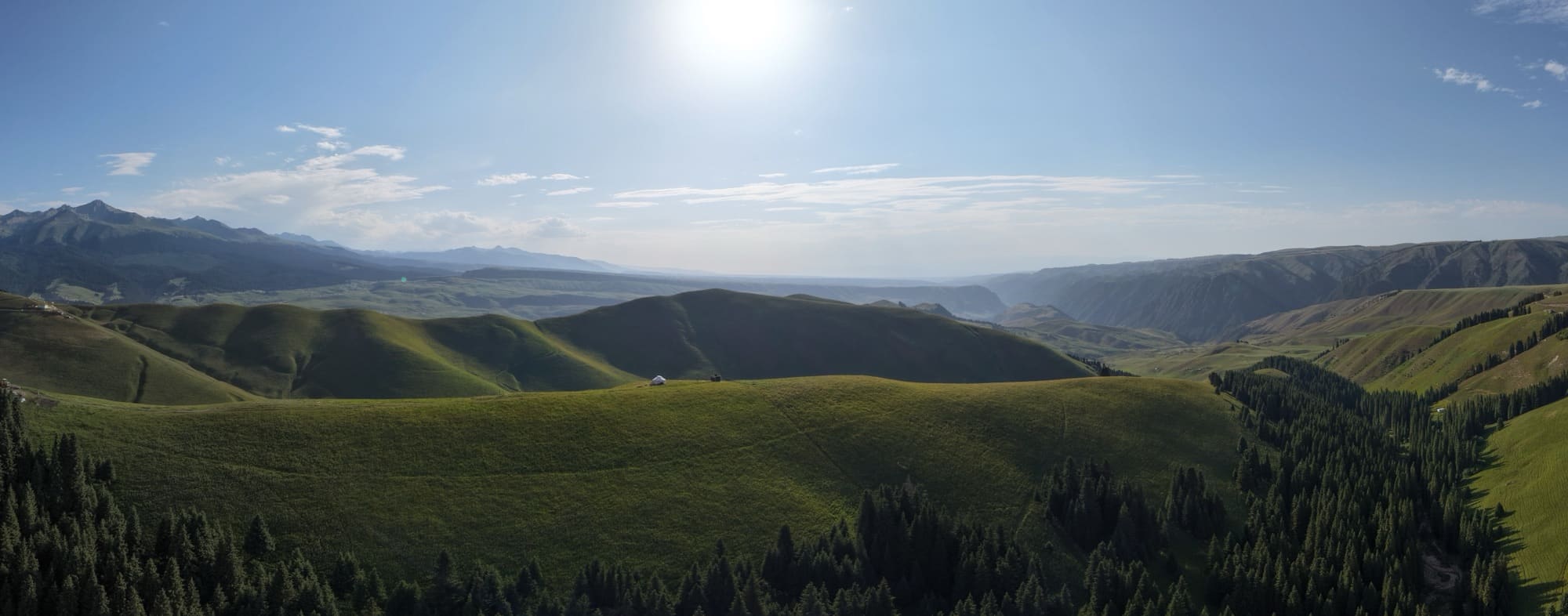 Stitched panorama sweeping across green ridges with the sun low overhead.
