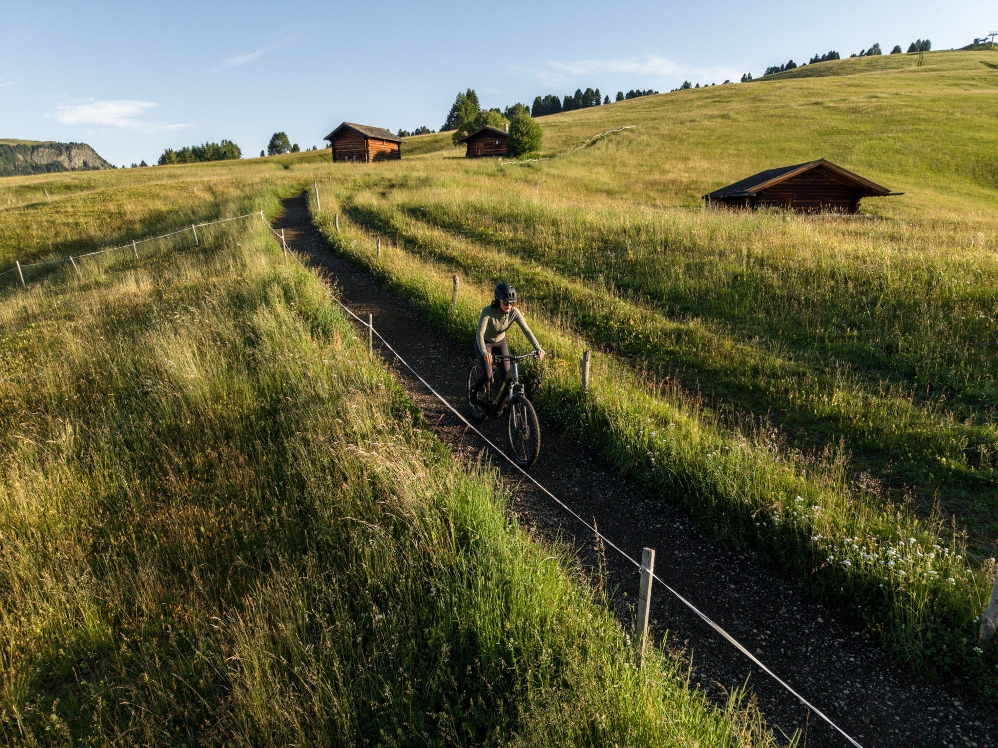 Aerial view of a lone cyclist on a gravel track winding past alpine barns.