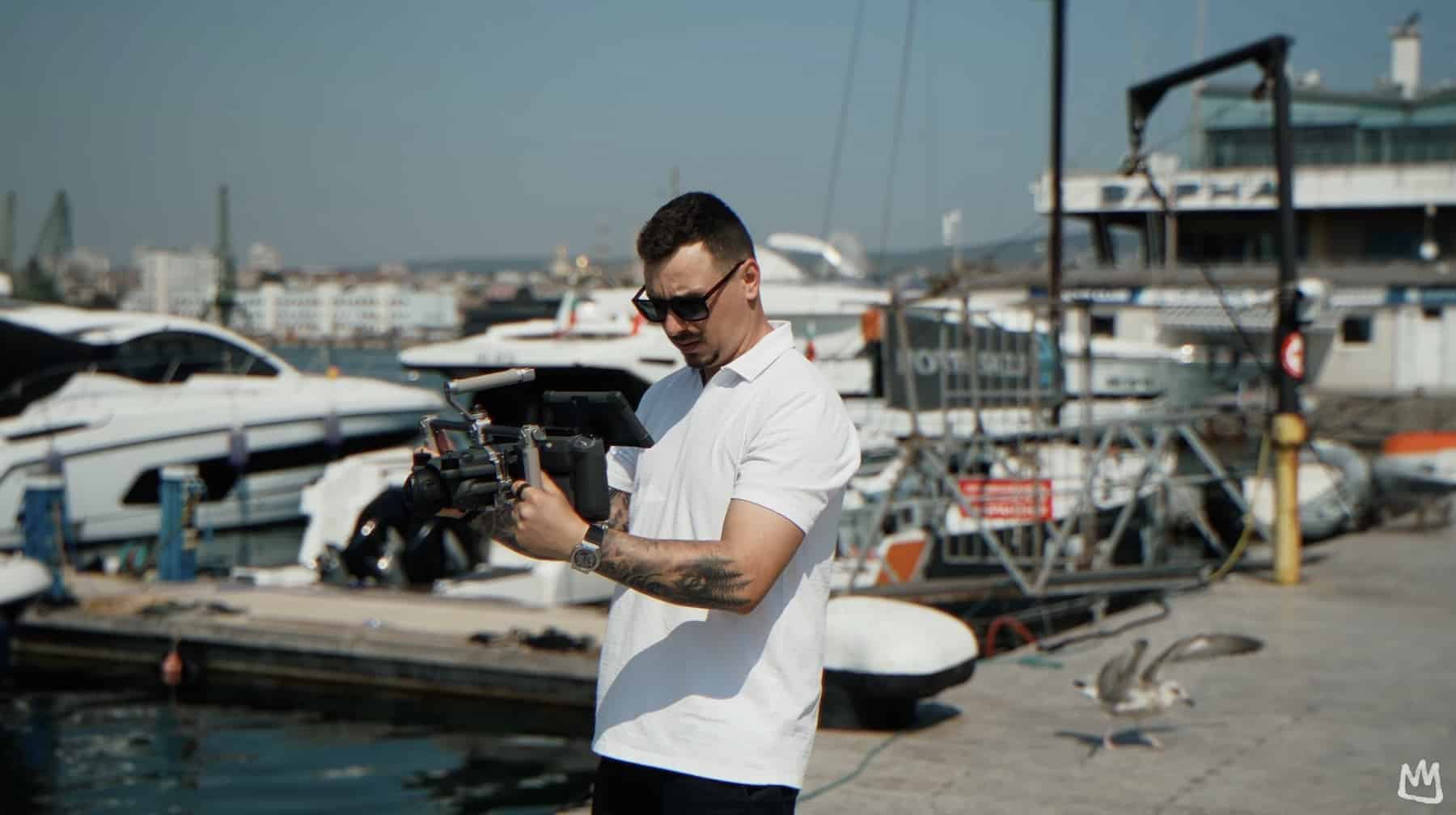 Operator in sunglasses holds the drone on its handle mount at a marina.