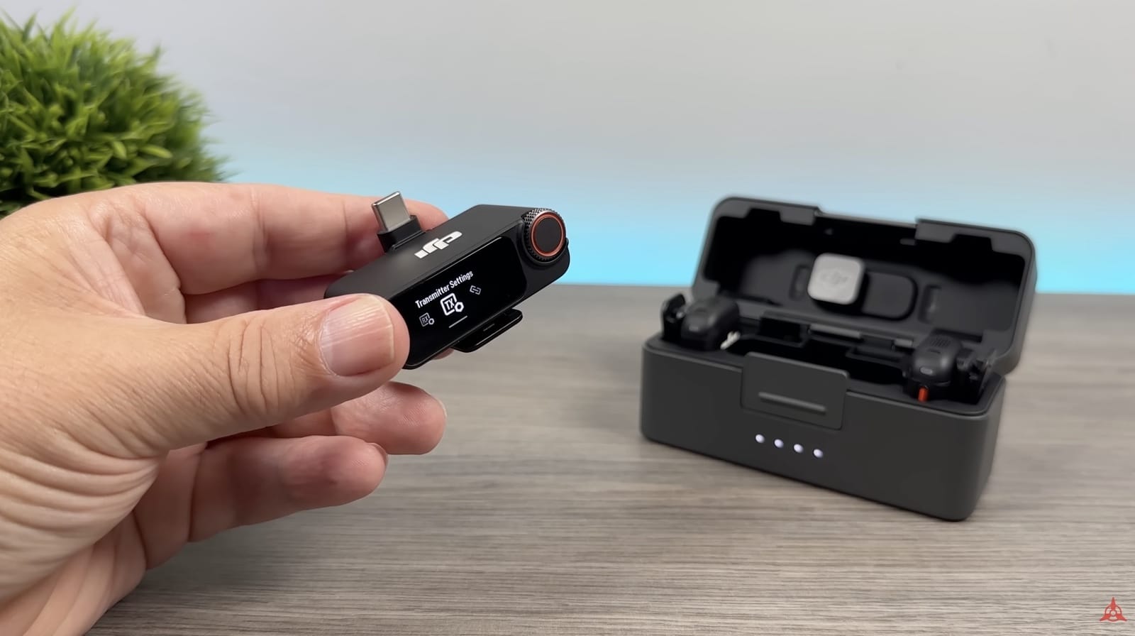 Hand holding the receiver with its USB-C adapter beside the open charging case.