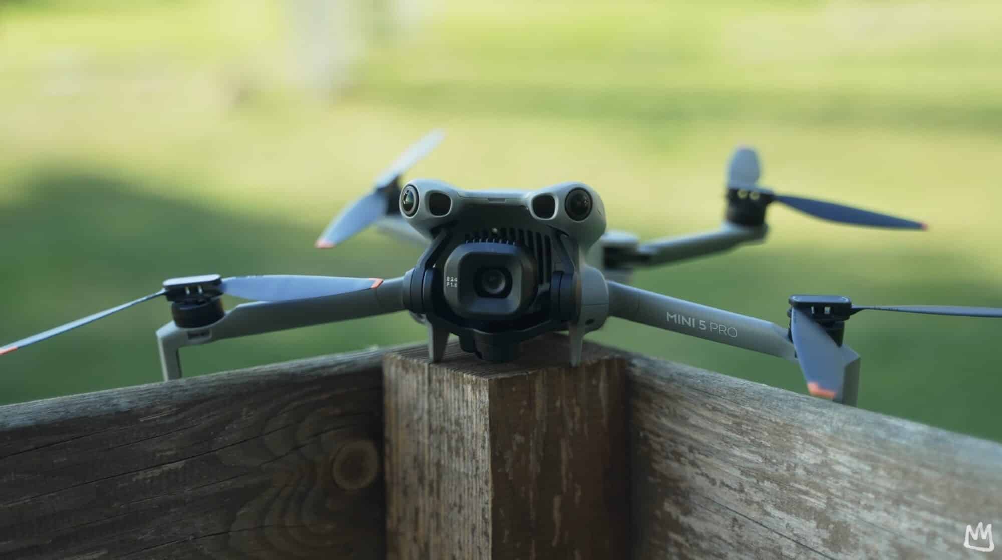 DJI Mini 5 Pro unfolded on a wooden fence post above a lawn.