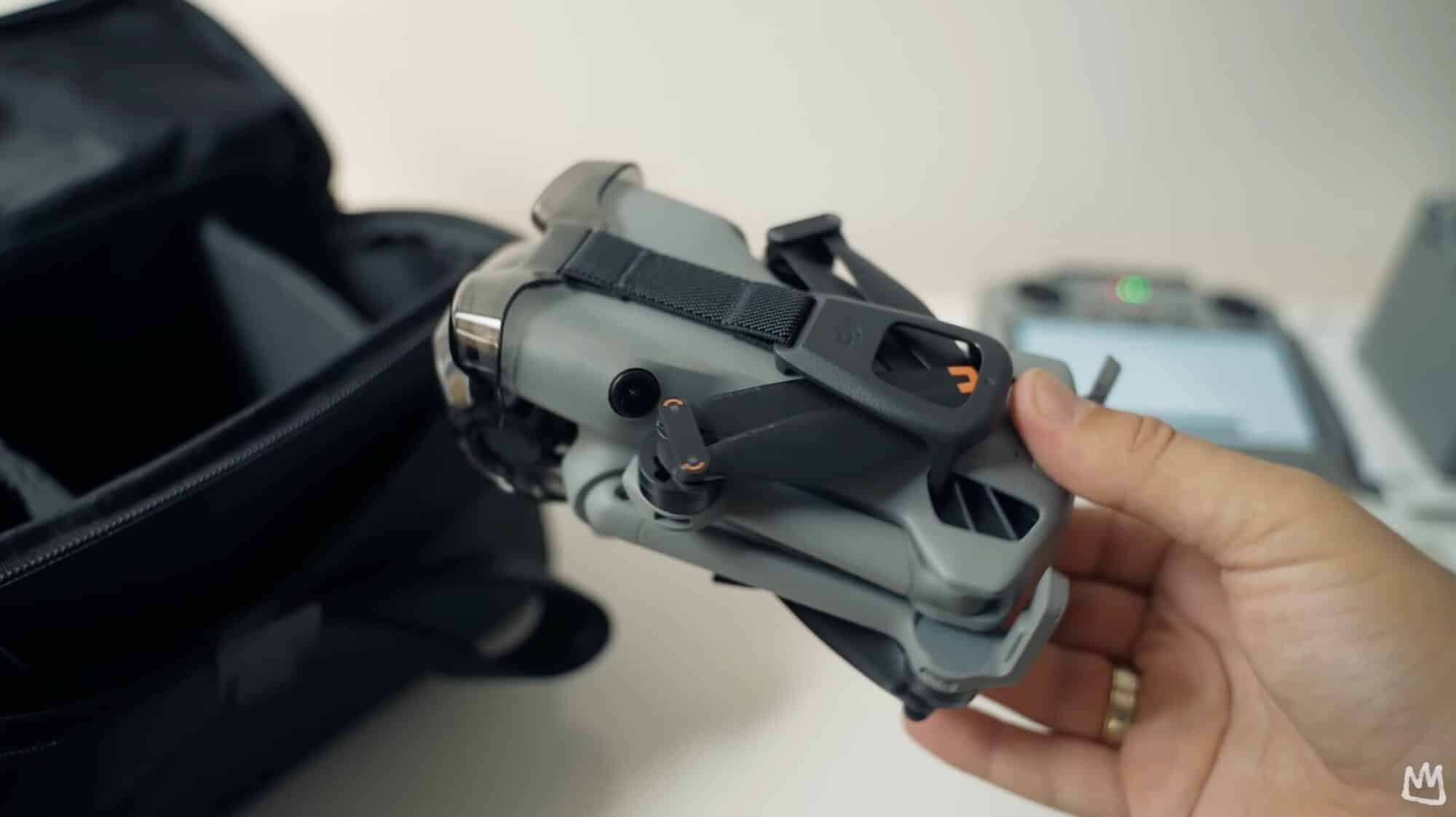 Hand holds the folded DJI Mini 5 Pro above its bag and controller.