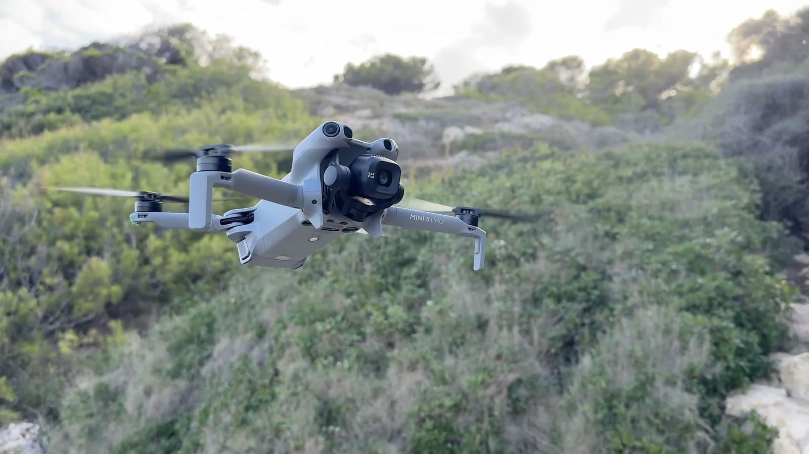 The DJI Mini 5 Pro hovering above coastal scrub during a test flight.