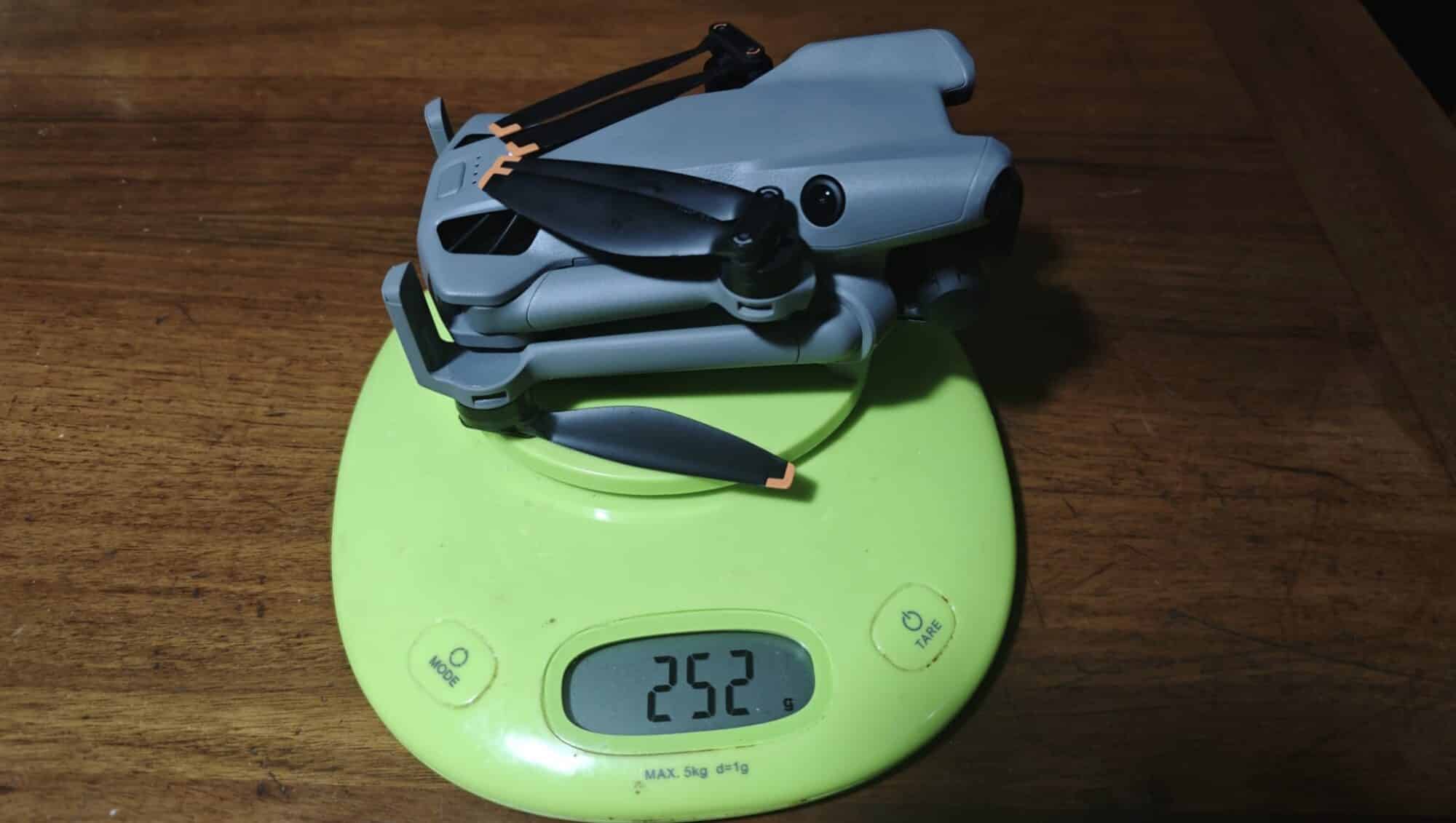 A folded gray DJI Mini 5 Pro on a green kitchen scale showing 252 grams.