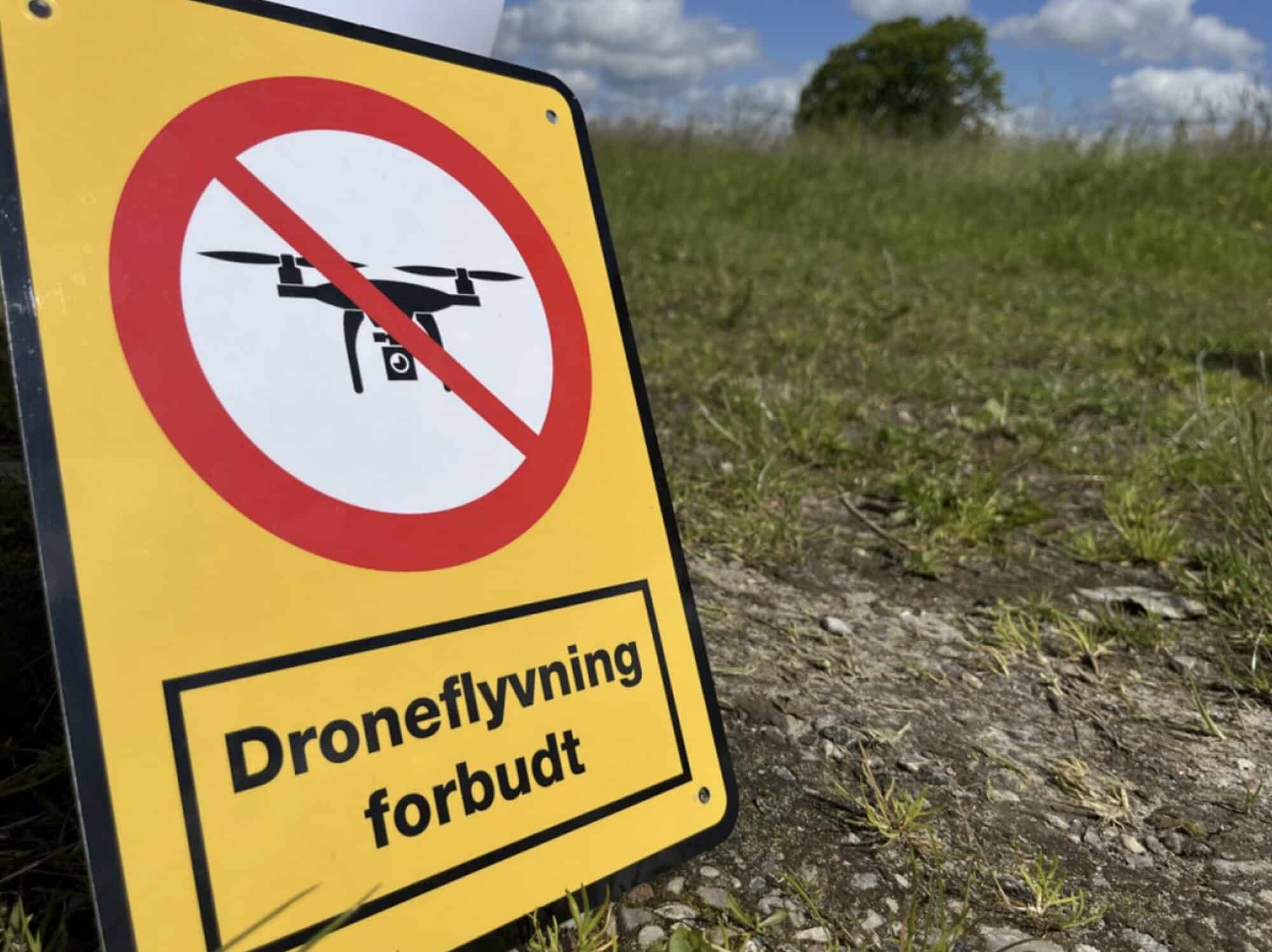 Yellow Danish sign in a field reading droneflyvning forbudt with a crossed-out drone.