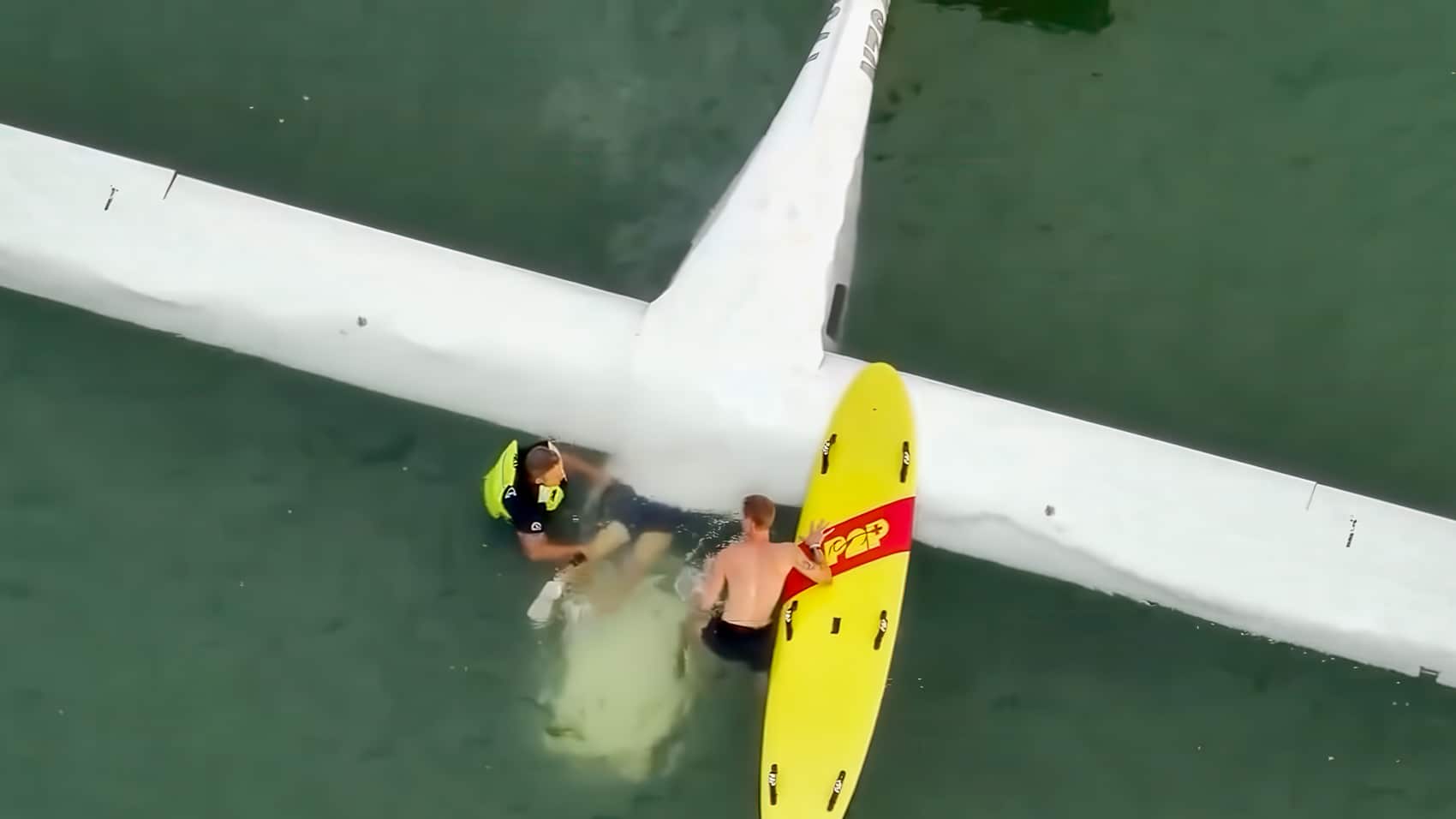 Drone view of a rescuer on a board reaching someone beside a downed aircraft wing.