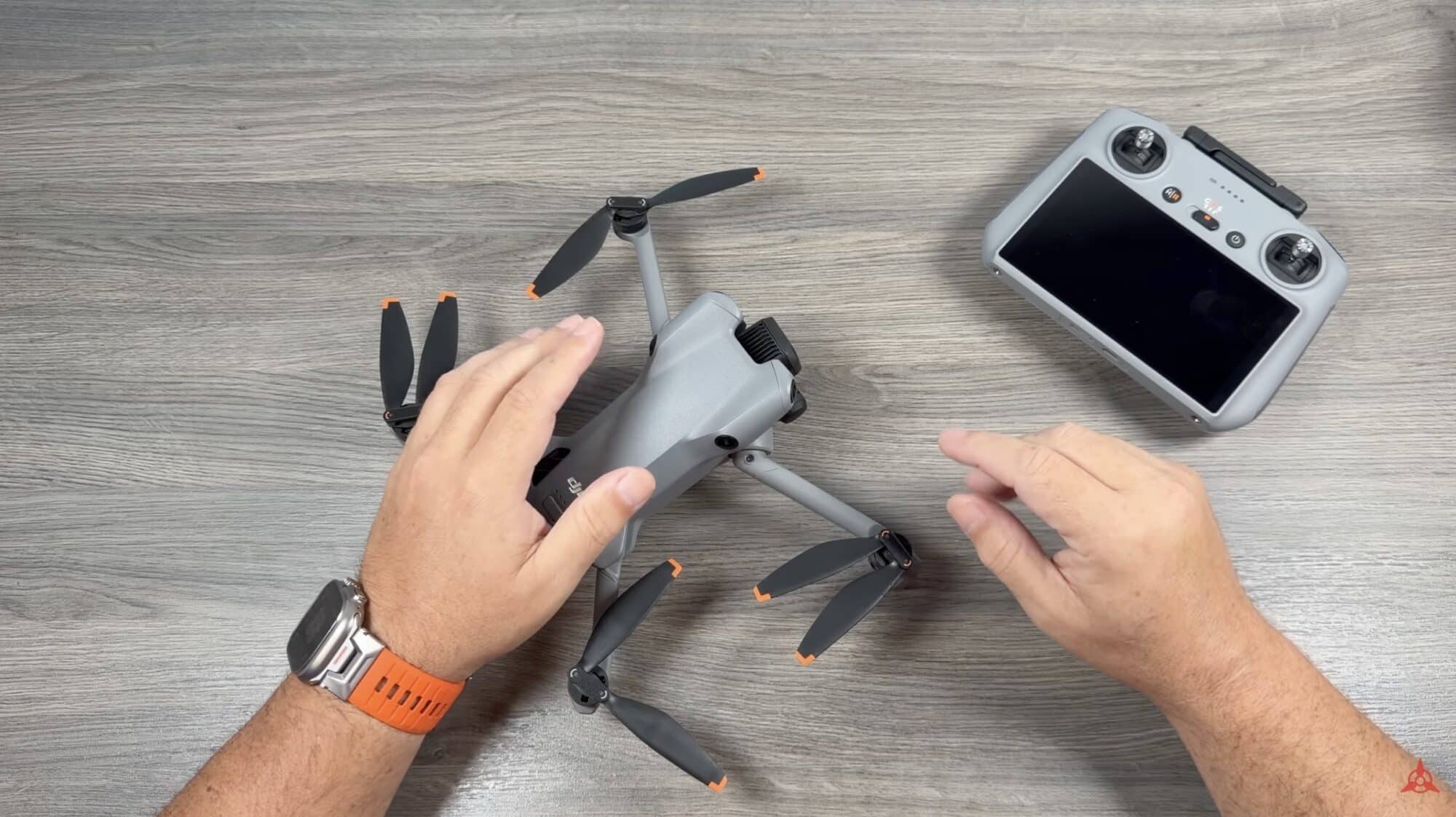 Hands unfold the Mini 5 Pro's arms on a desk beside the RC 2 controller.