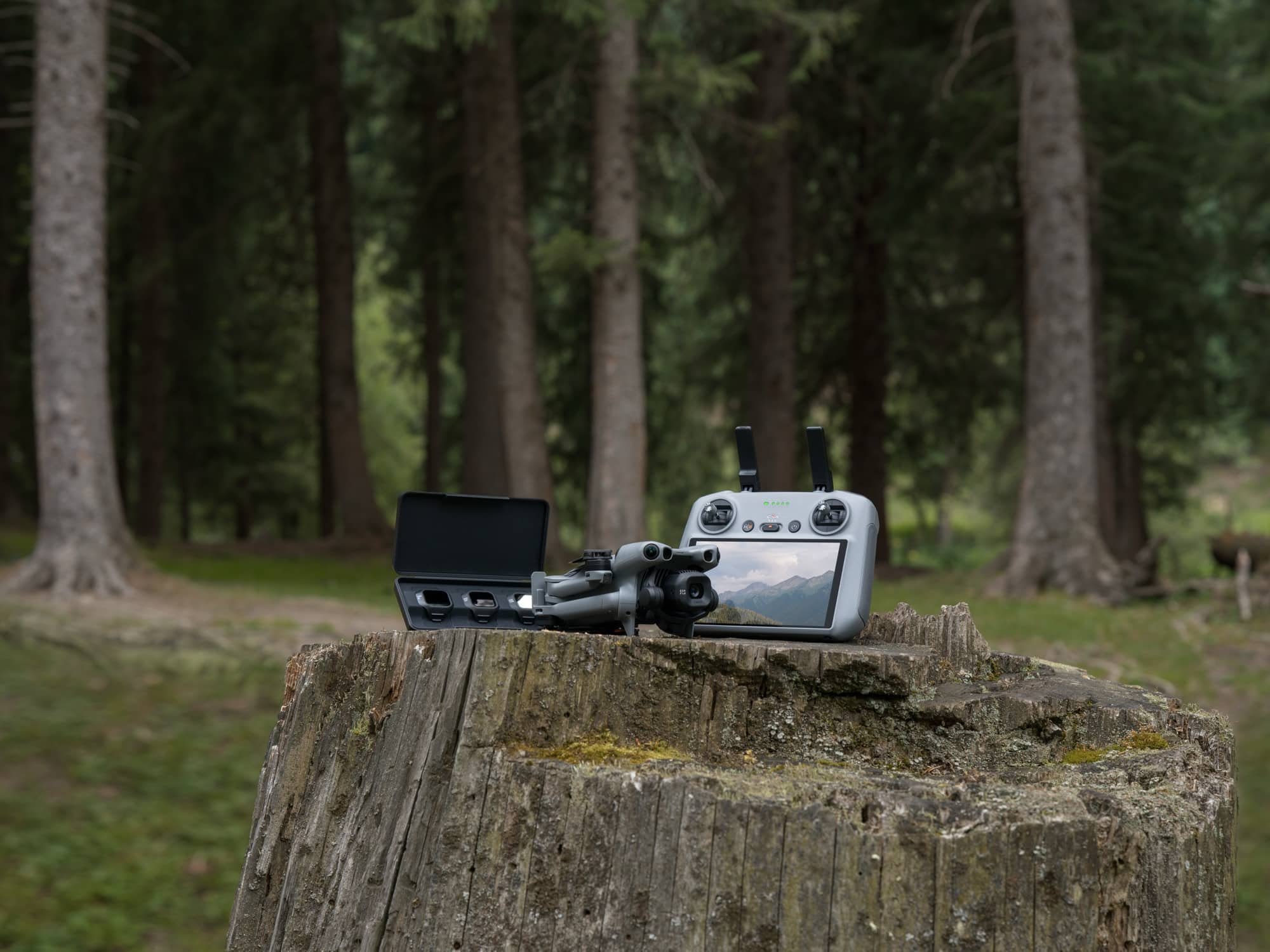 Folded drone beside a touchscreen controller resting on a weathered stump among pines.