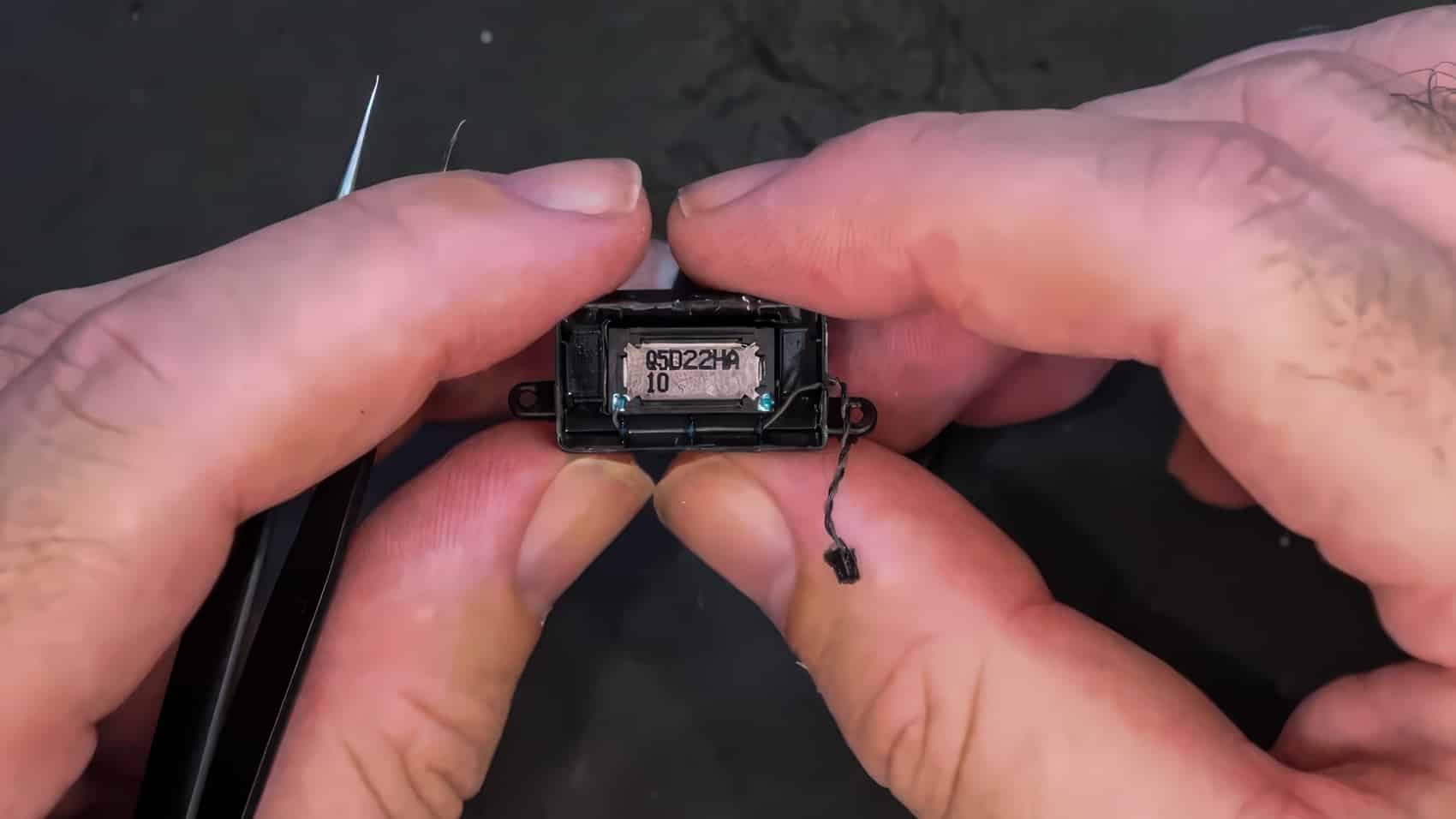 Fingertips hold the tiny speaker module pulled from the drone's fuselage.