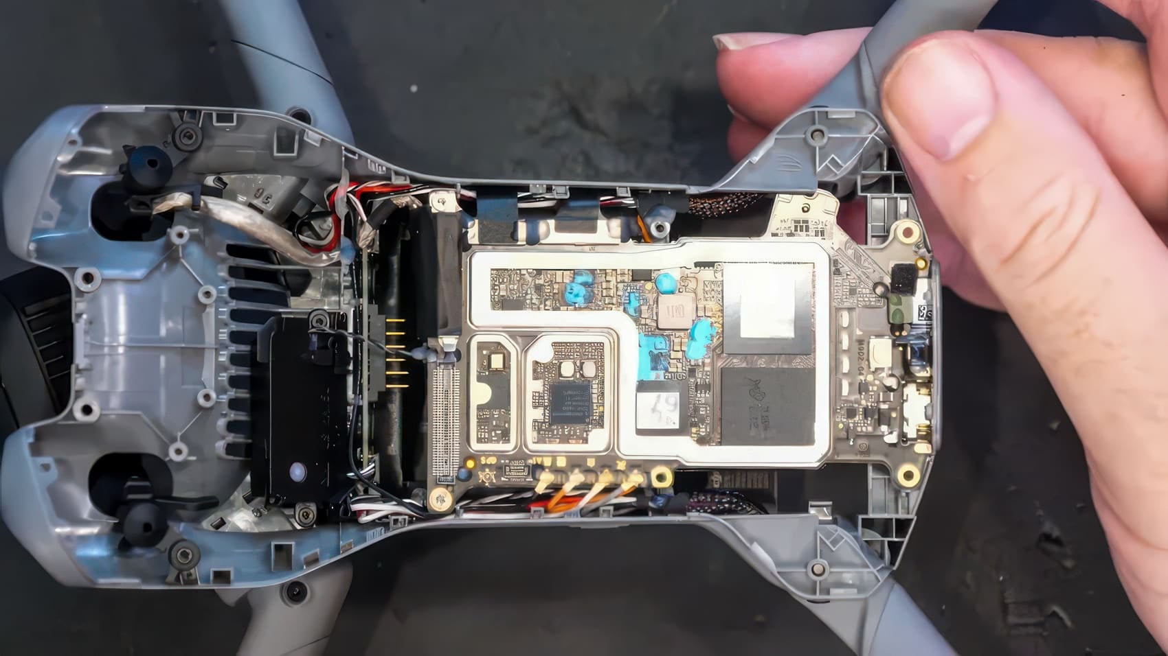 Hands hold an opened DJI Mini 5 Pro shell, exposing its main circuit board.