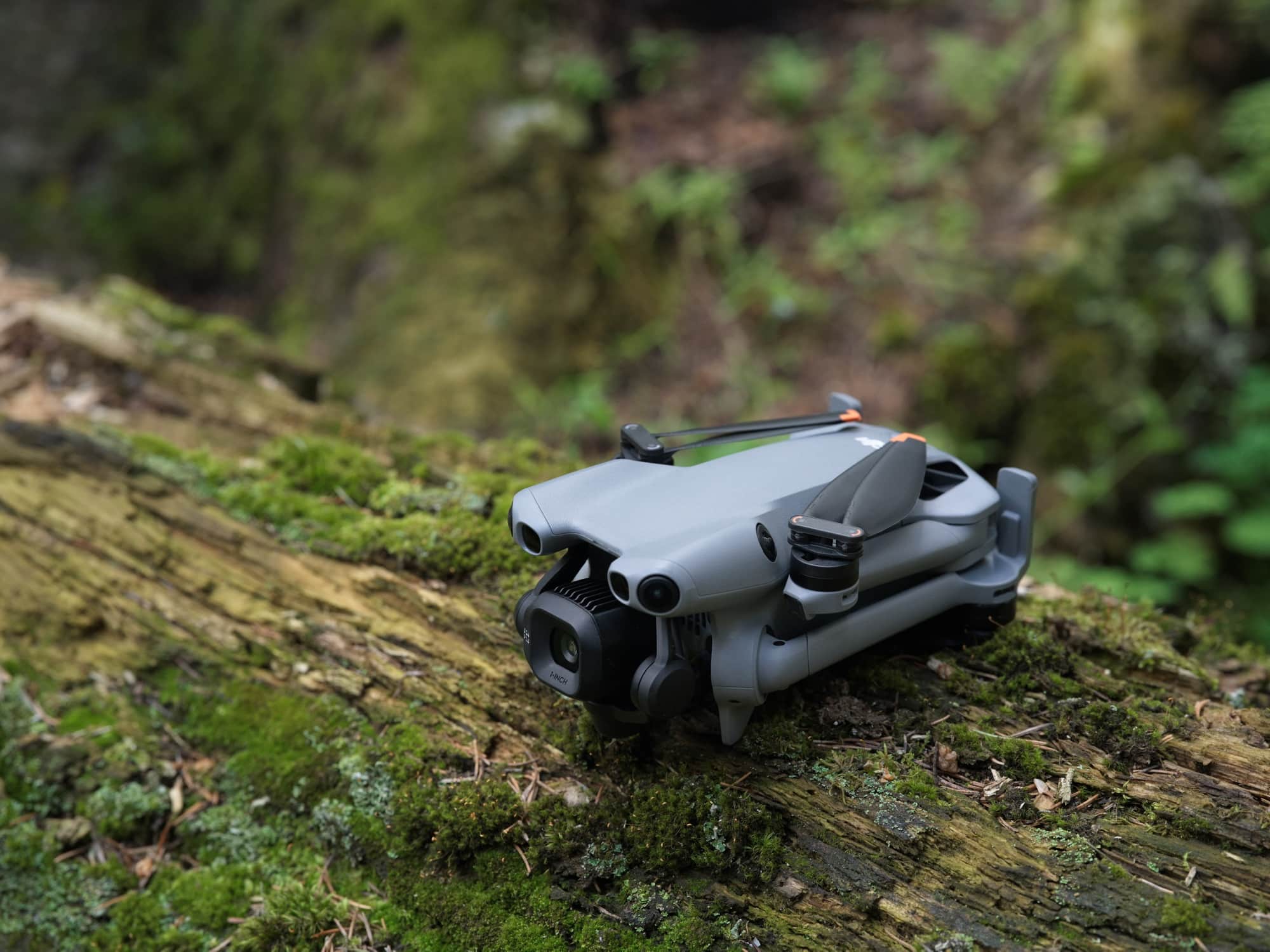 The folded drone rests on a moss-covered log with its arms tucked in.