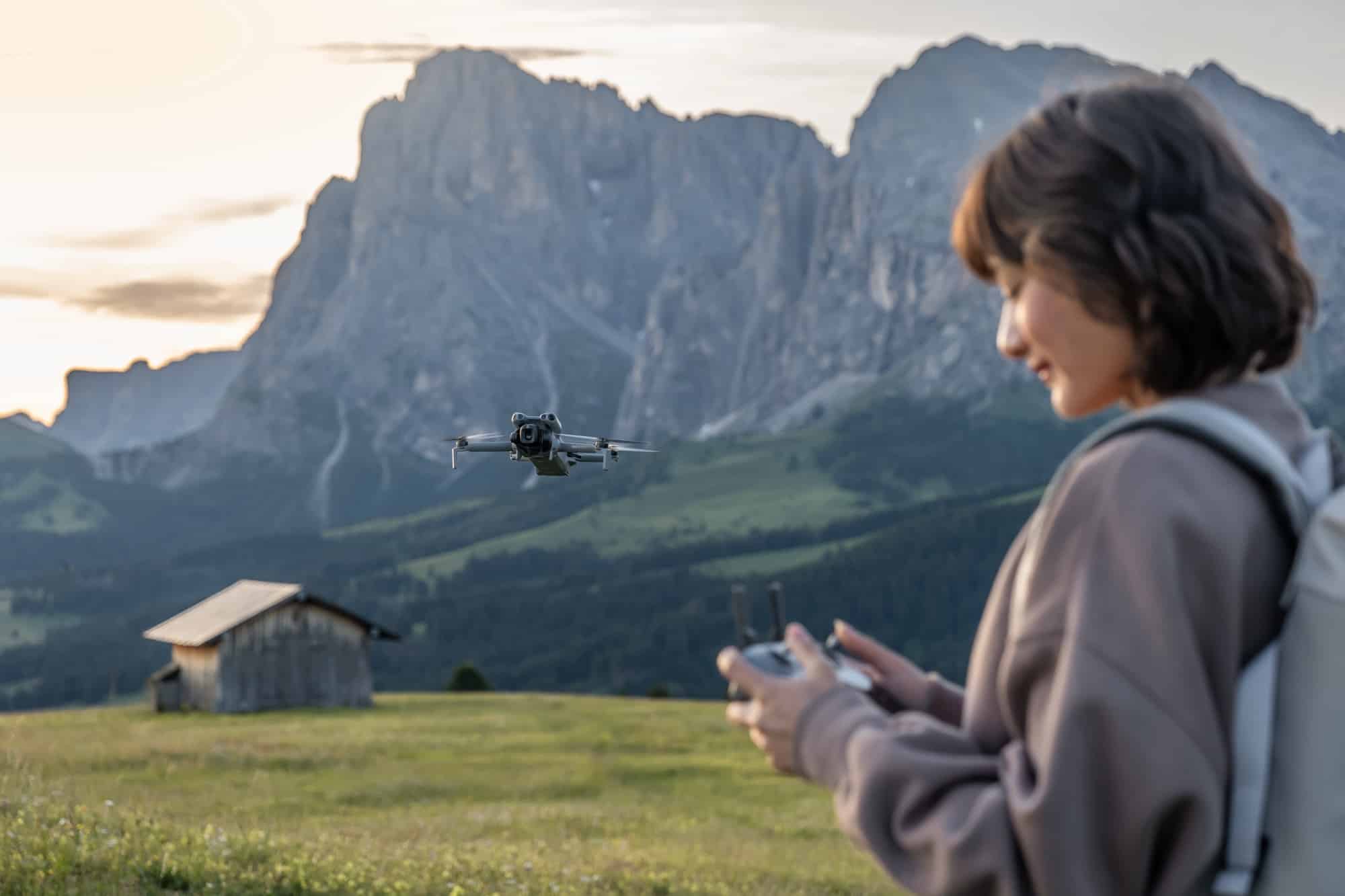 A hiker with a backpack flies the drone in front of a dolomite massif at dusk.