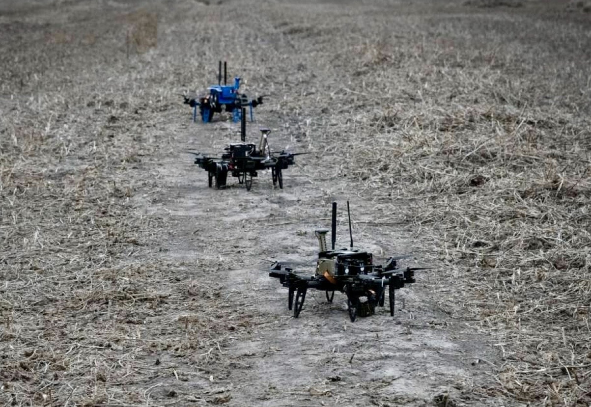 Two small strike drones sitting on dry winter grass in an open field.