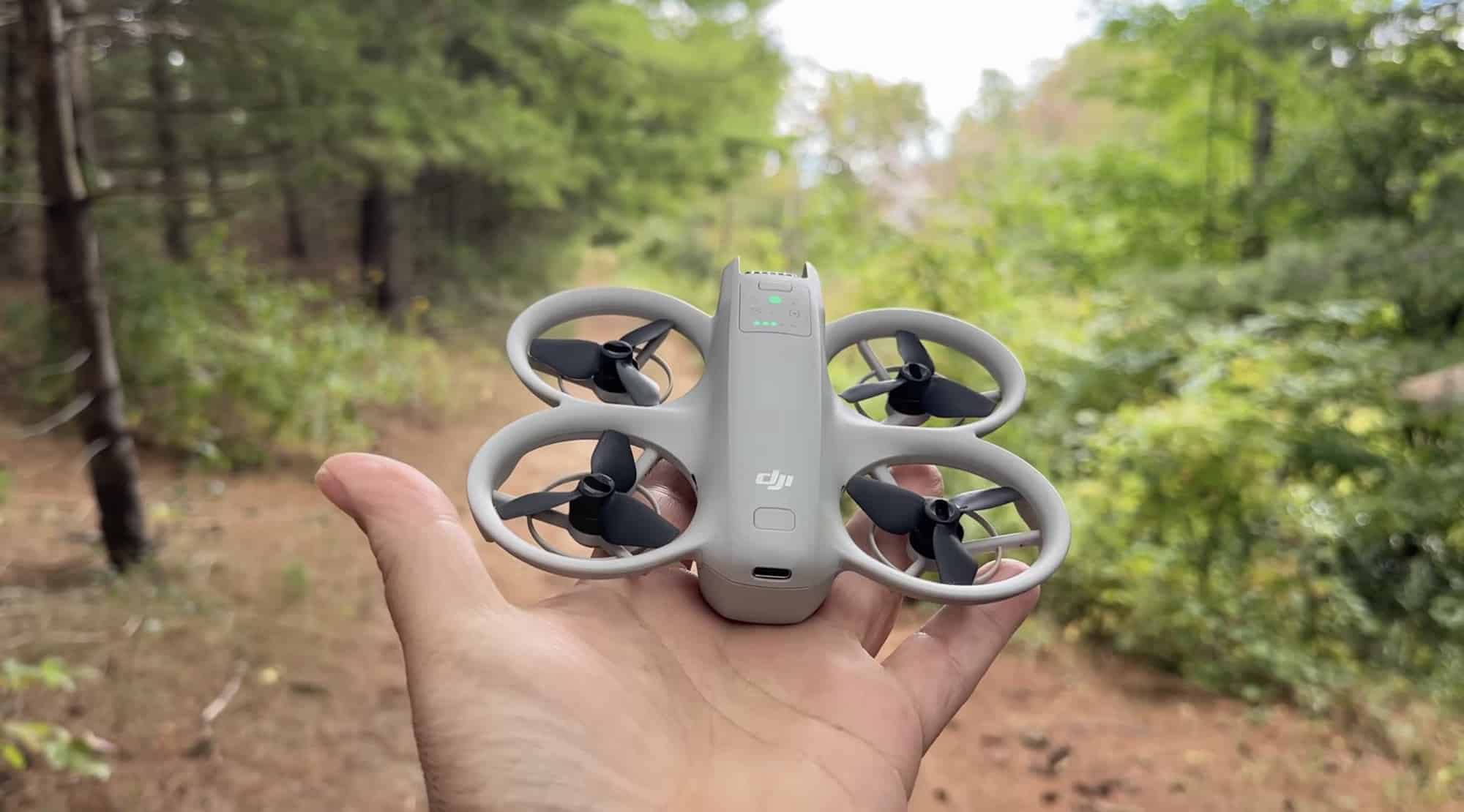 An open palm holds the DJI Neo on a sunlit forest trail.