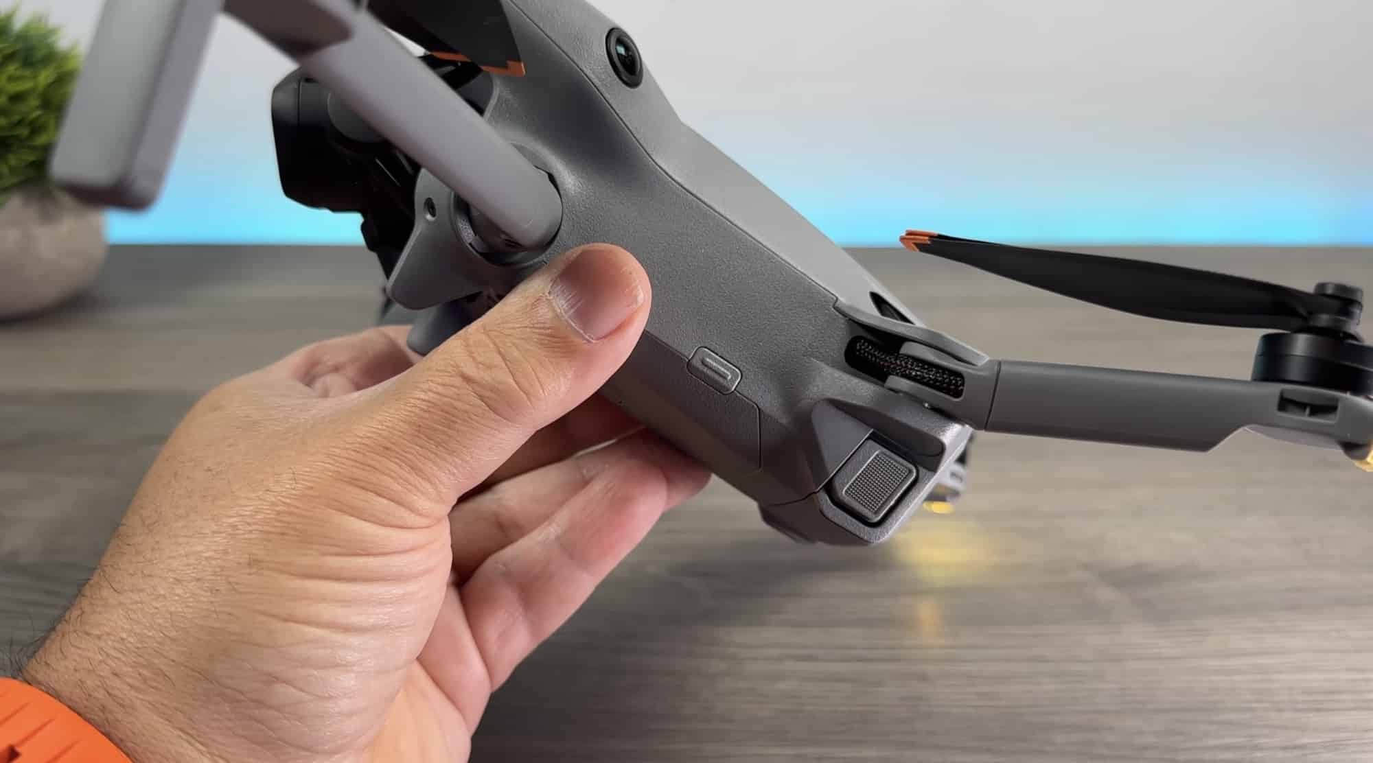 Hands unfold the drone's rear arms on a wooden tabletop.