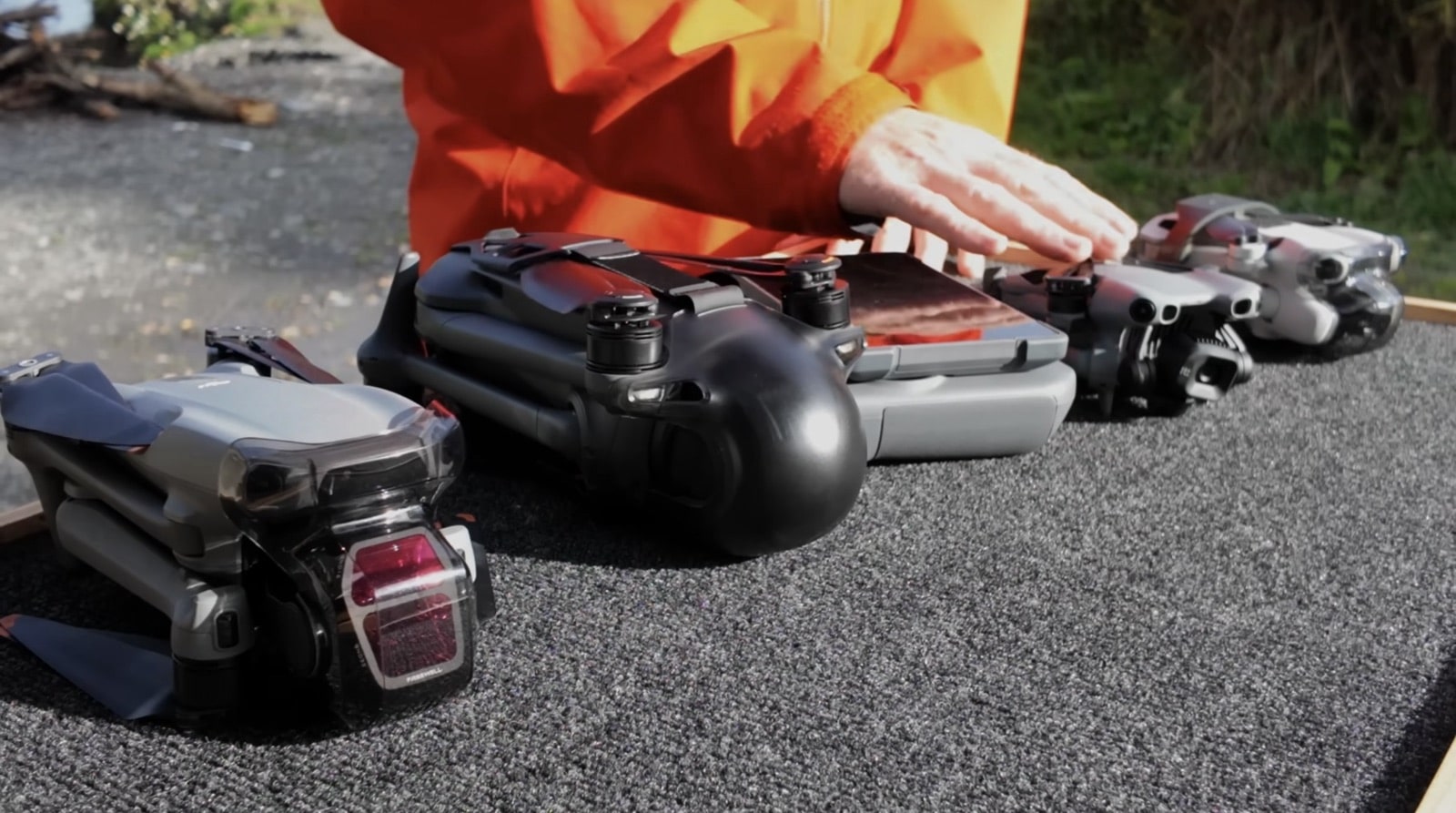 Hands lining up several folded DJI drones and controllers on pavement.