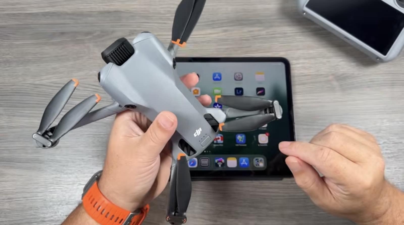 Hands holding the folded Mini 5 Pro above an iPad home screen.
