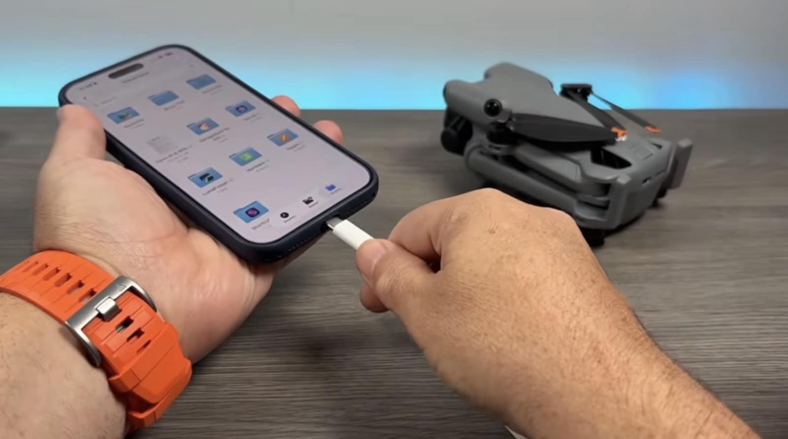 Hand holding a phone and a USB-C cable next to the folded drone.