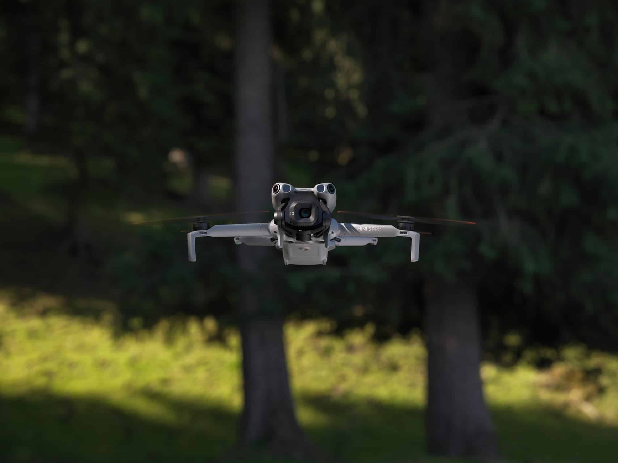The drone hangs among dark conifers, propellers blurred and gimbal angled toward the camera.