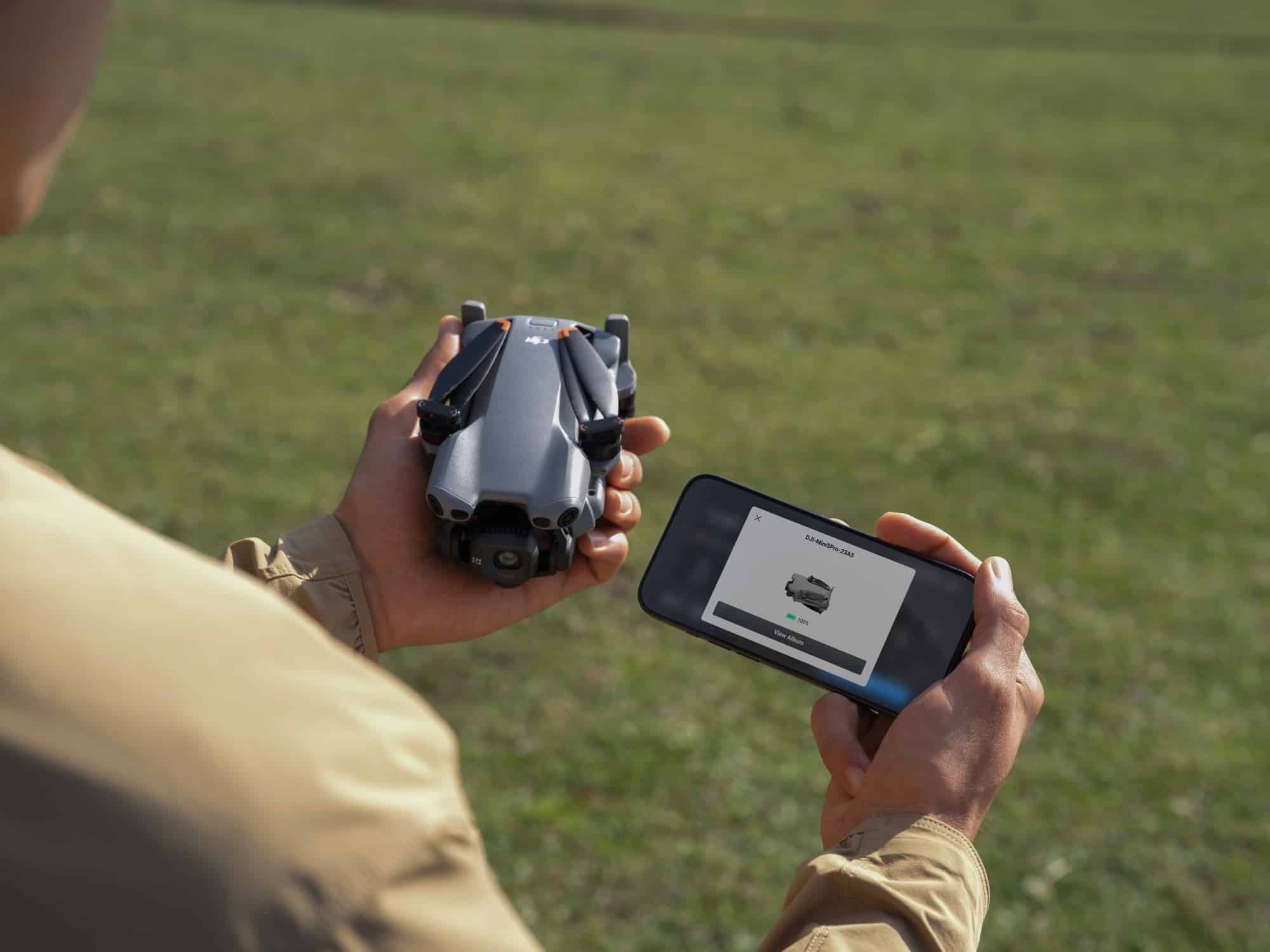 Hands hold the folded drone beside a phone showing the wireless footage transfer screen.