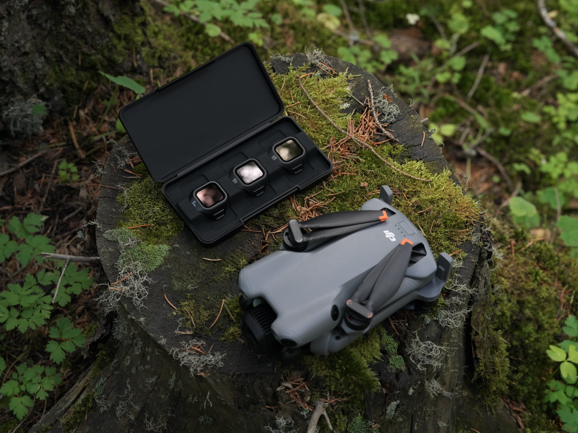 An open case holding three ND filters lies on moss beside the folded drone.