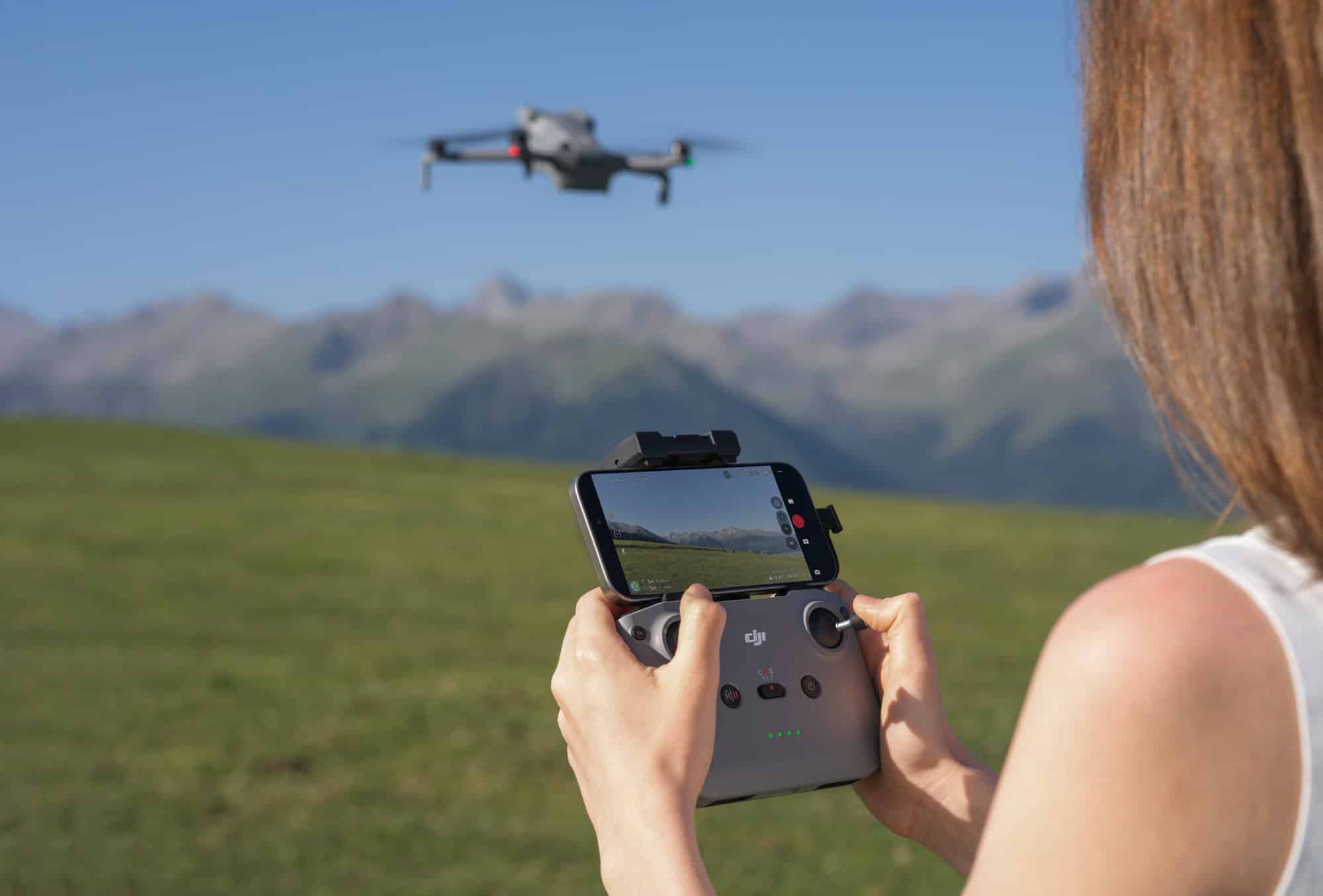 A woman grips the RC-N3 controller with a phone clipped above it, drone hovering ahead.