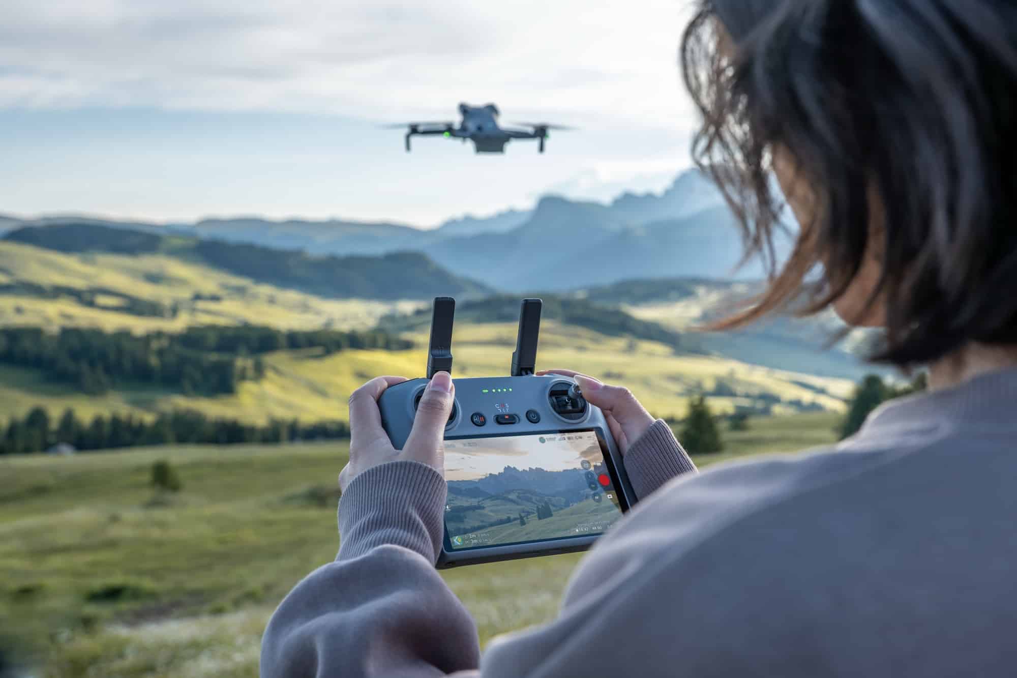 Over-the-shoulder view of the controller screen with the drone small against distant hills.