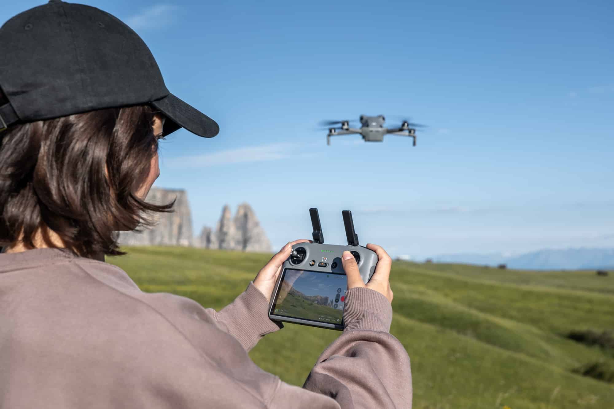 A woman in a black cap holds the RC 2 controller as the drone hovers overhead.