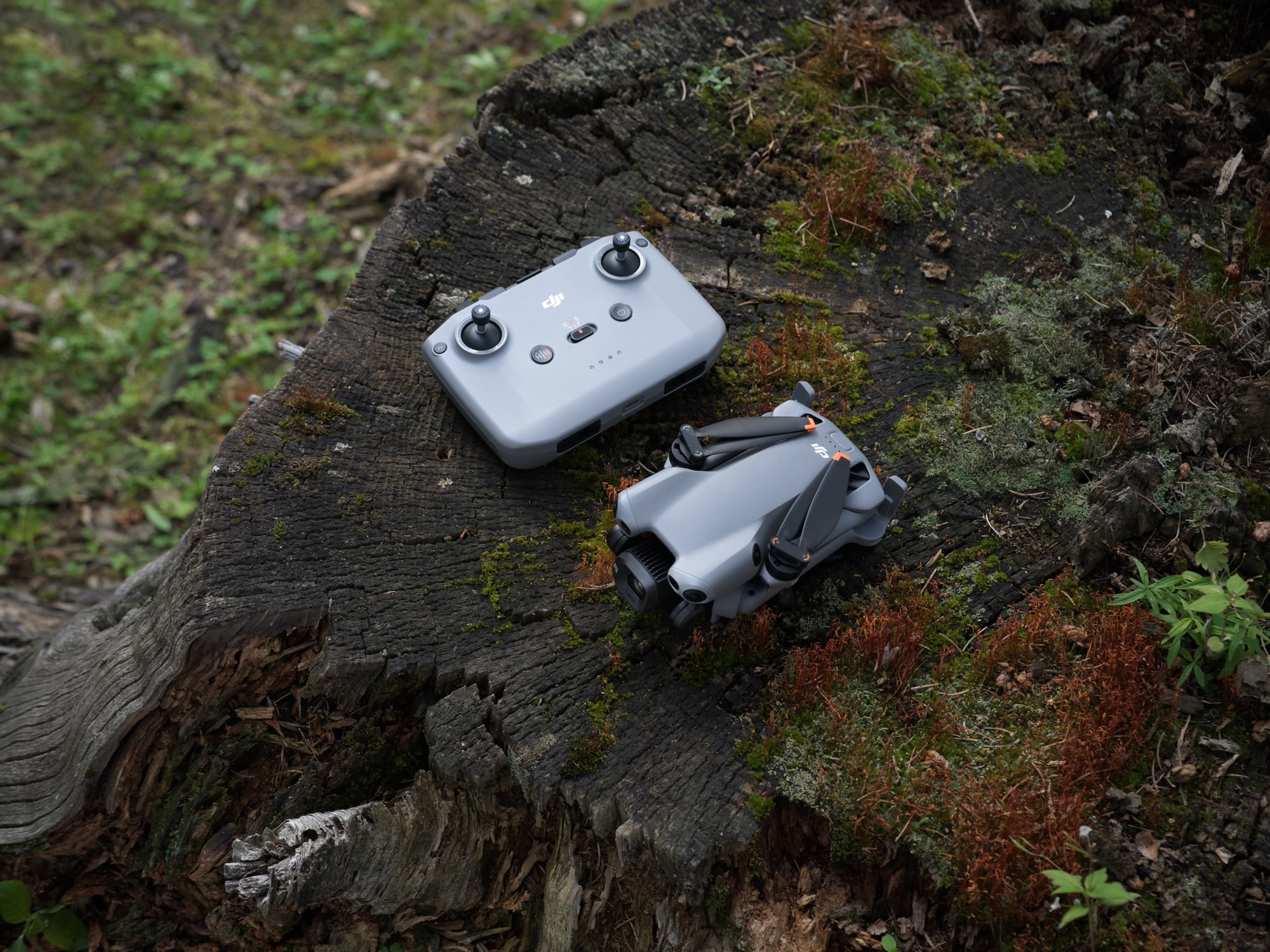 Folded drone and plain RC-N3 controller arranged together on a lichen-covered log.