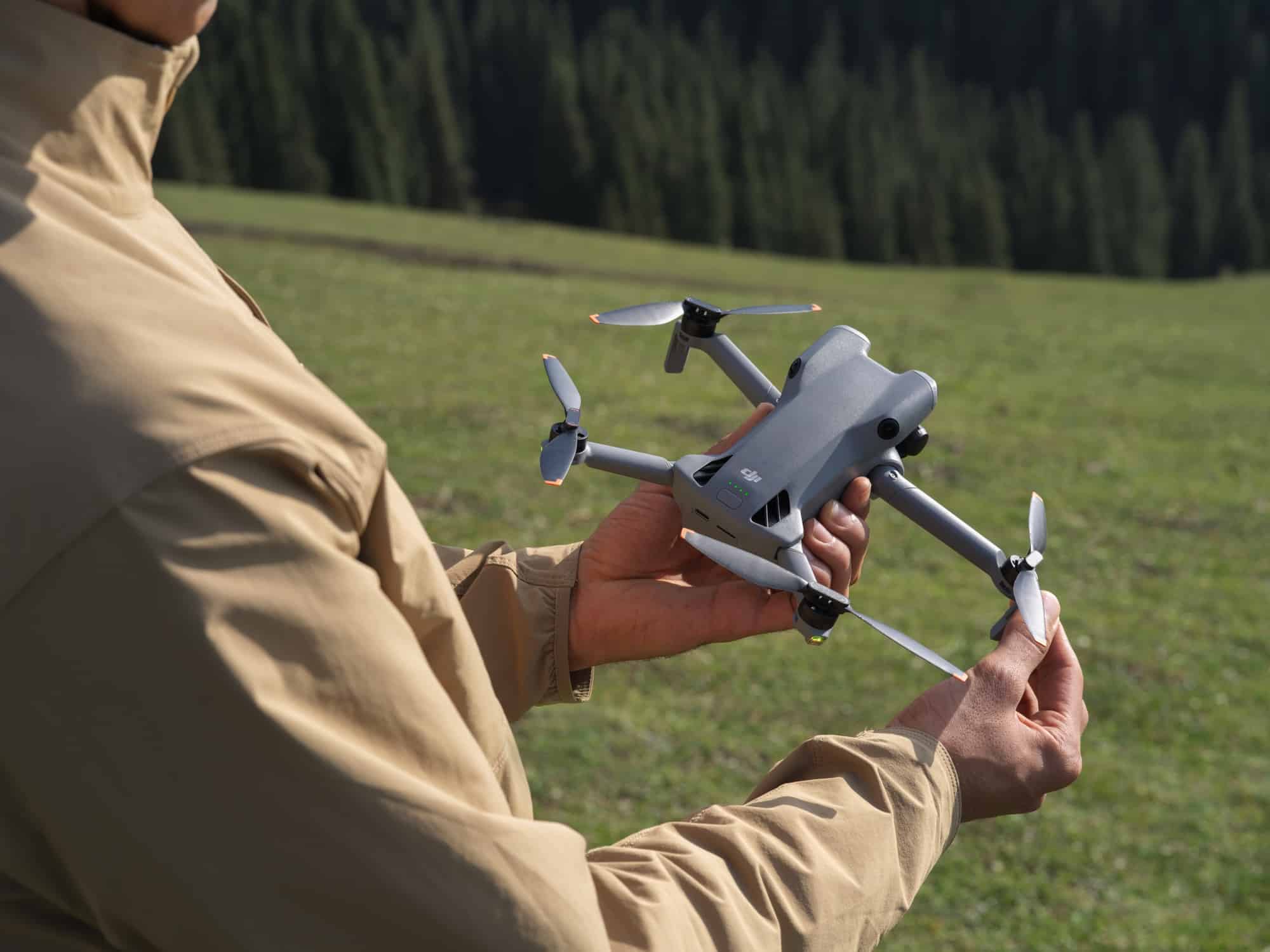 Two hands unfold the drone's rear arms while standing in a green meadow.