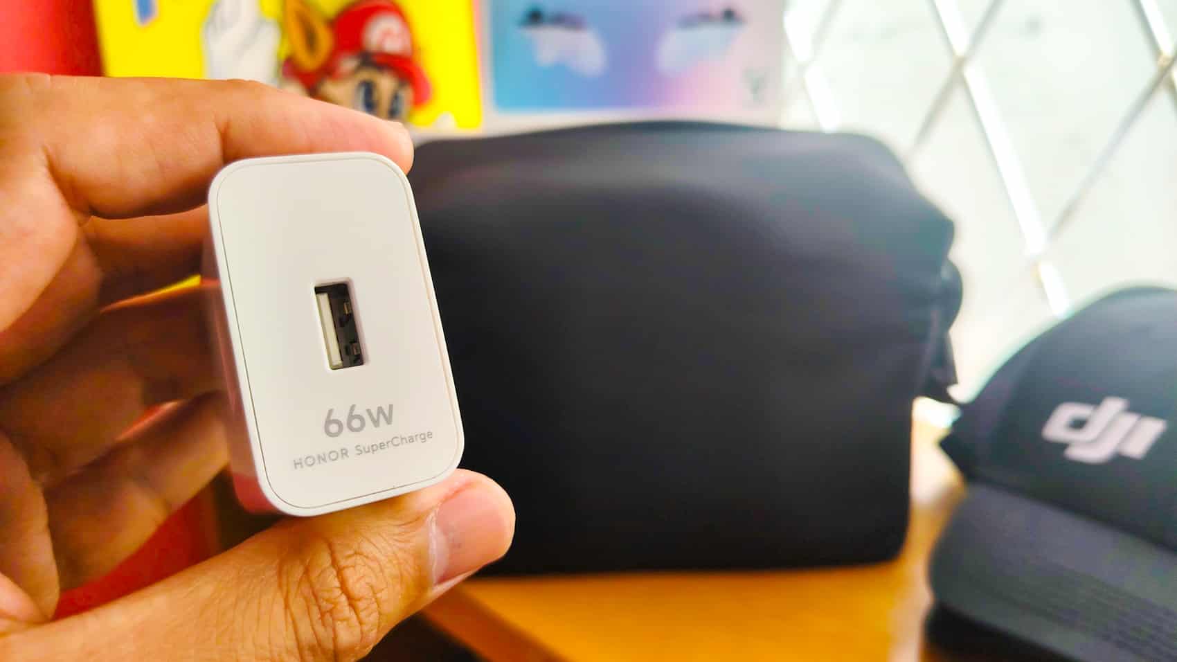 Hand holding a white 66-watt USB wall charger next to a DJI bag.