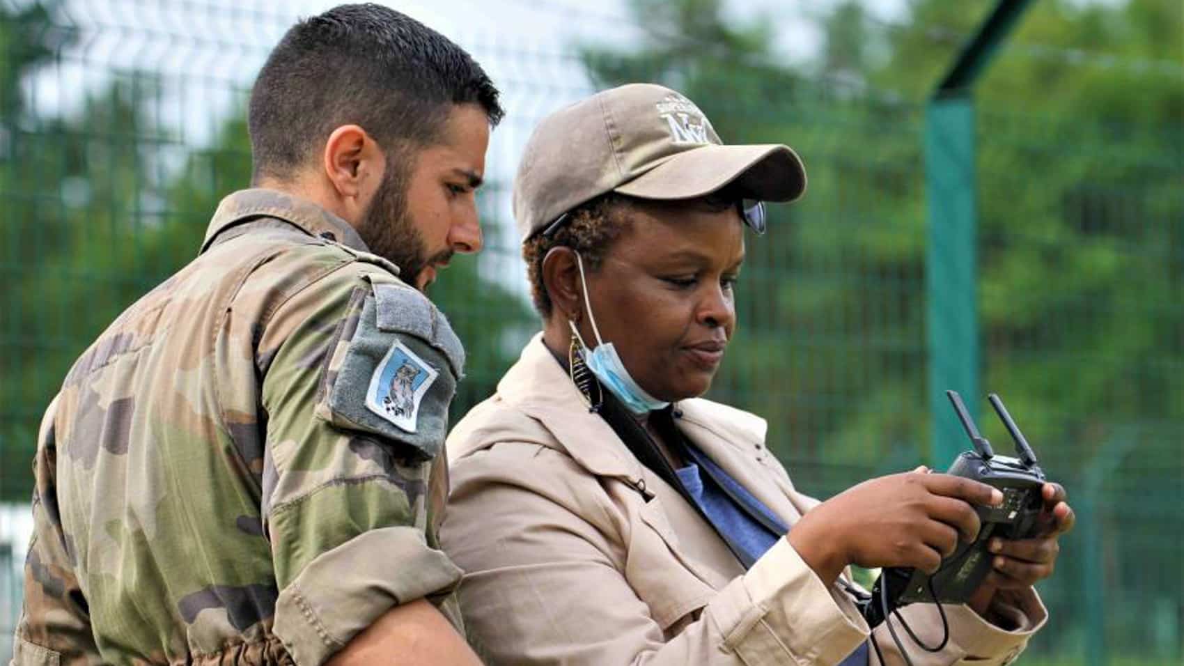 Instructor guides a woman peacekeeper flying a drone with a handheld controller.
