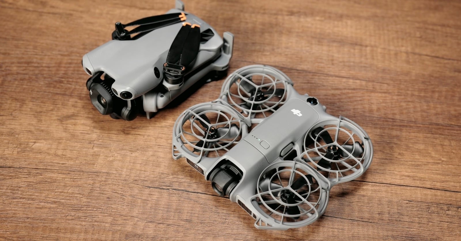 A folded DJI Mini 5 Pro sits on a wooden table next to the NEO 2.
