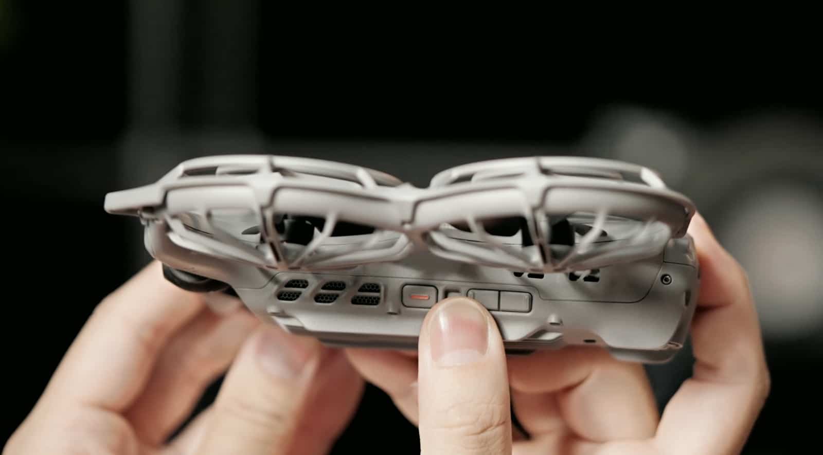 A thumb rests beside the orange-marked power button on the drone underside.