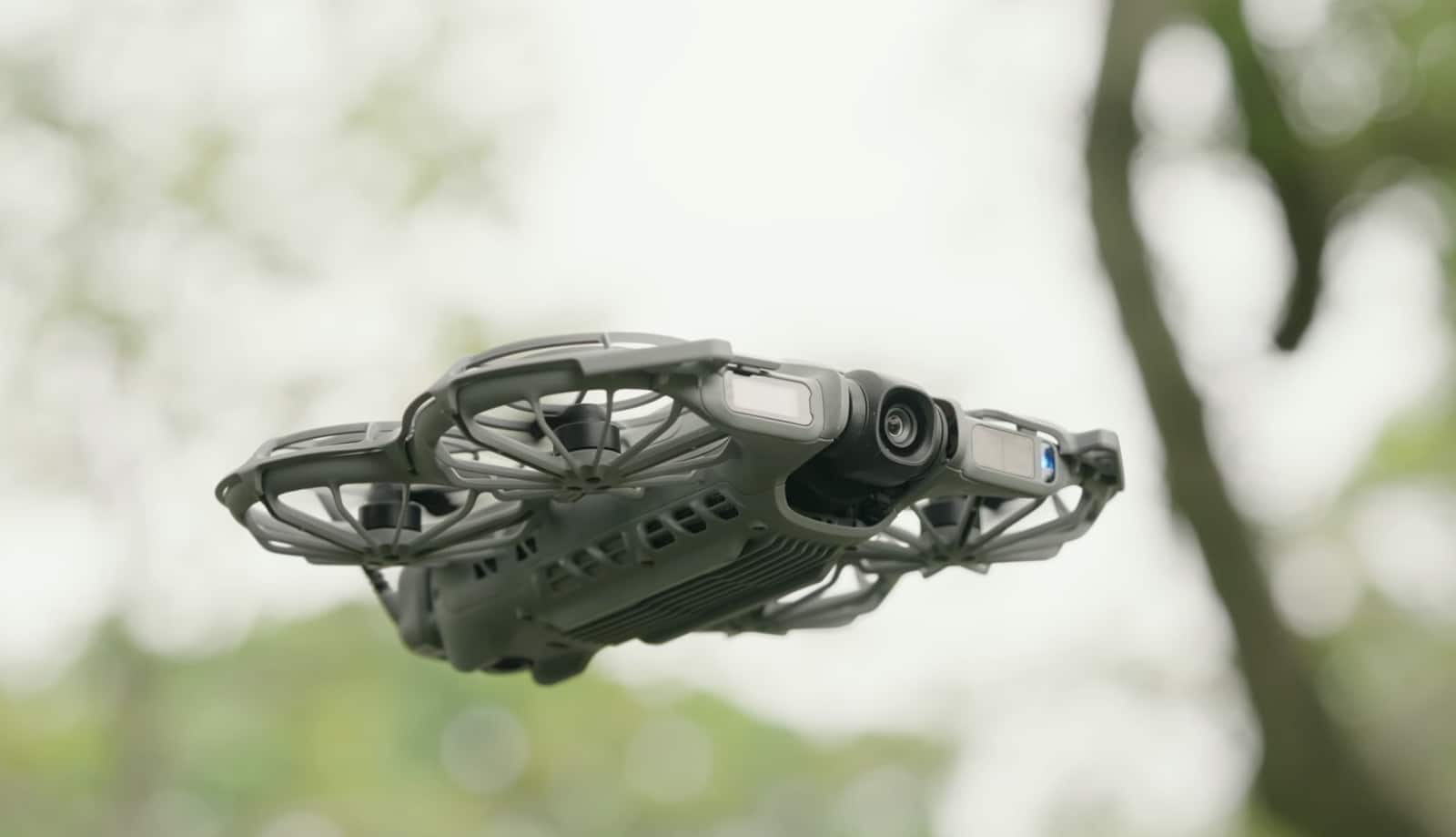 The NEO 2 hovers beside leafy branches against a bright overcast sky.