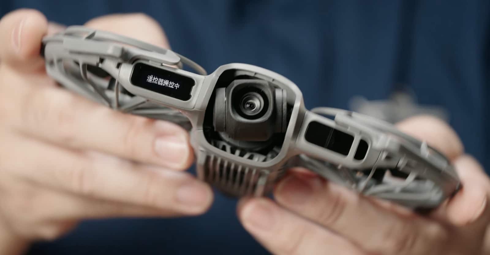 Both hands cradle the drone, its small front screen showing Chinese shooting settings.