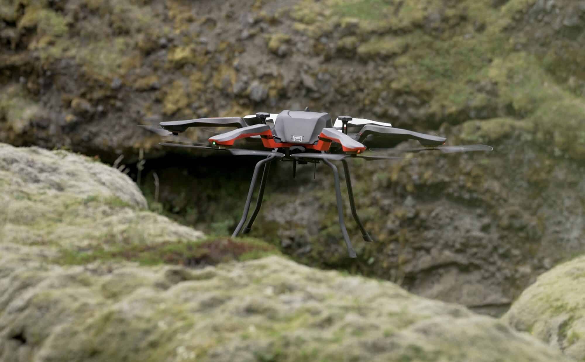 White and orange Acecore multirotor hovering low over moss-covered volcanic rock.