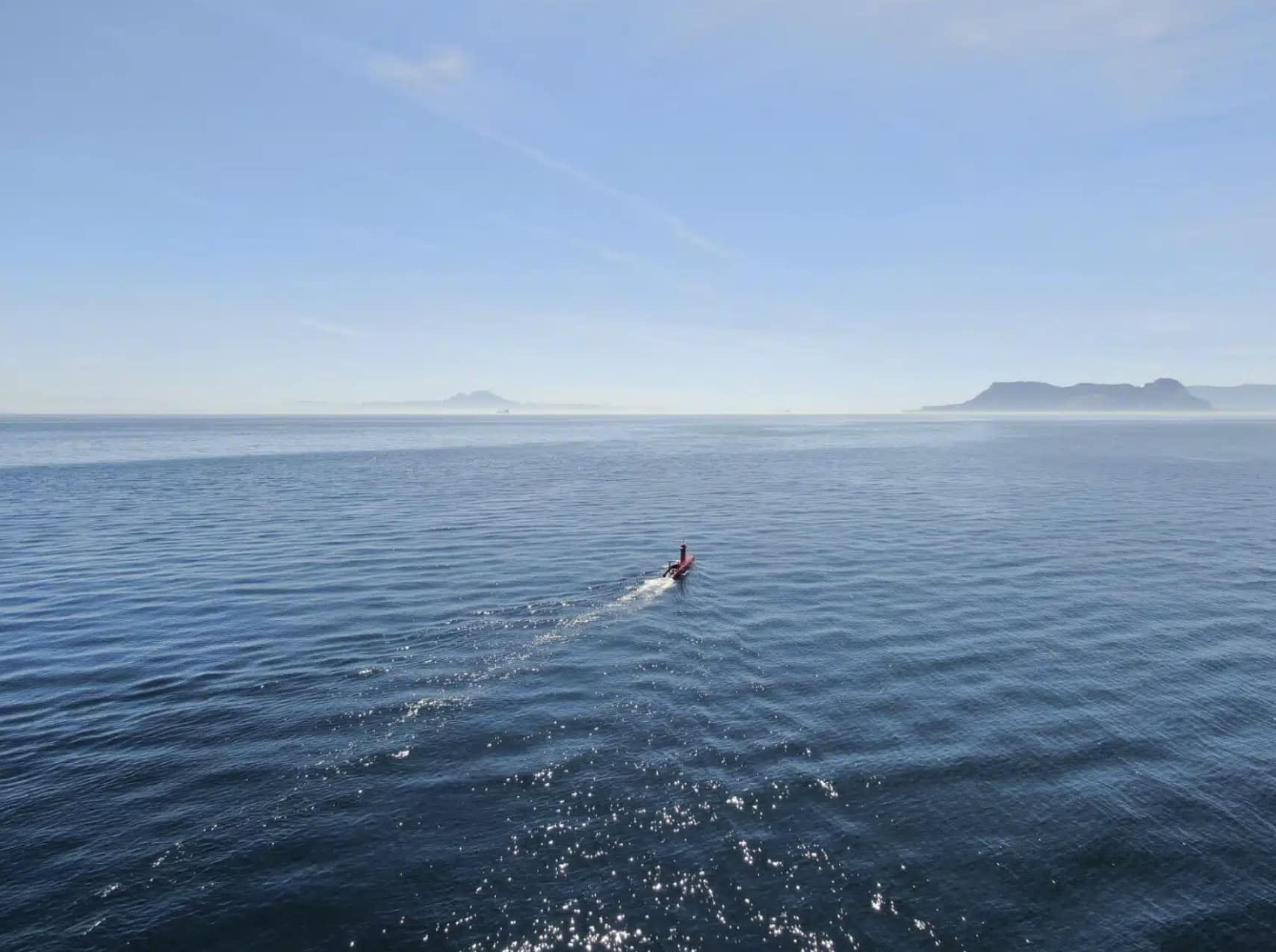 Unmanned surface vessel cutting across open sea toward a distant headland.