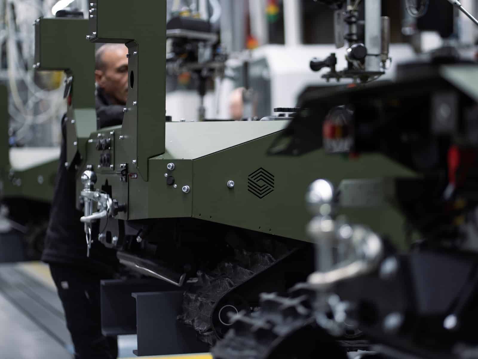 Technicians working on a tracked military ground robot inside a factory.