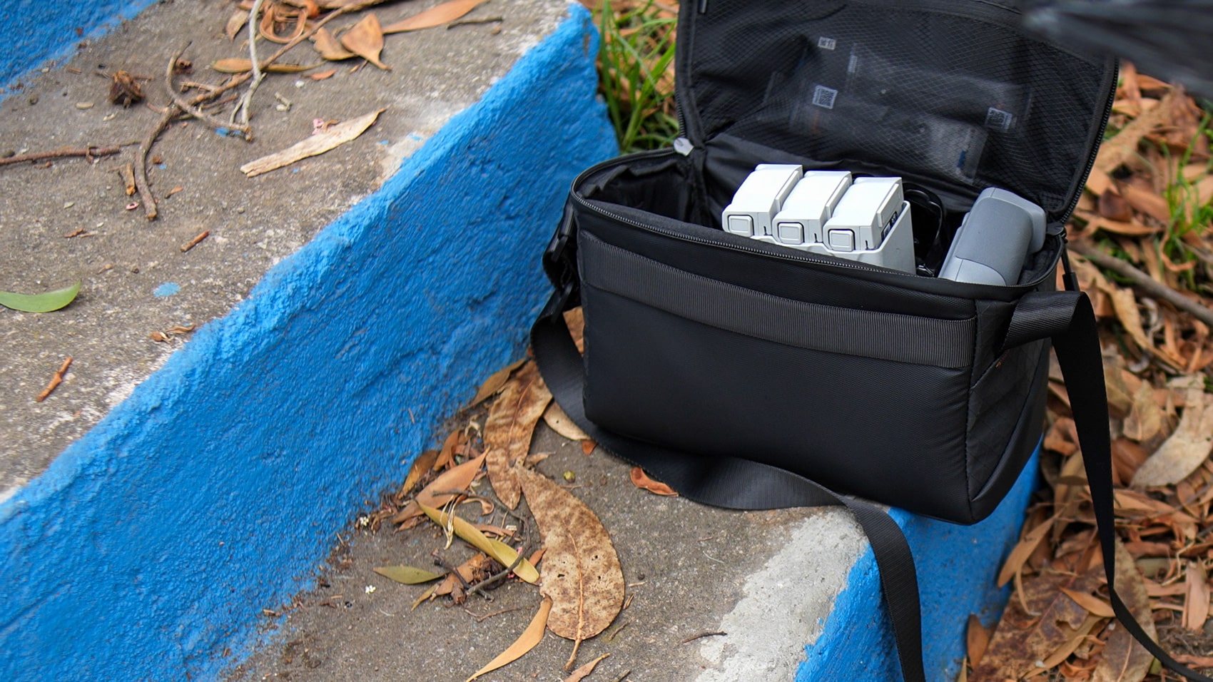 Shoulder bag on a painted curb holding drone batteries and a folded aircraft.