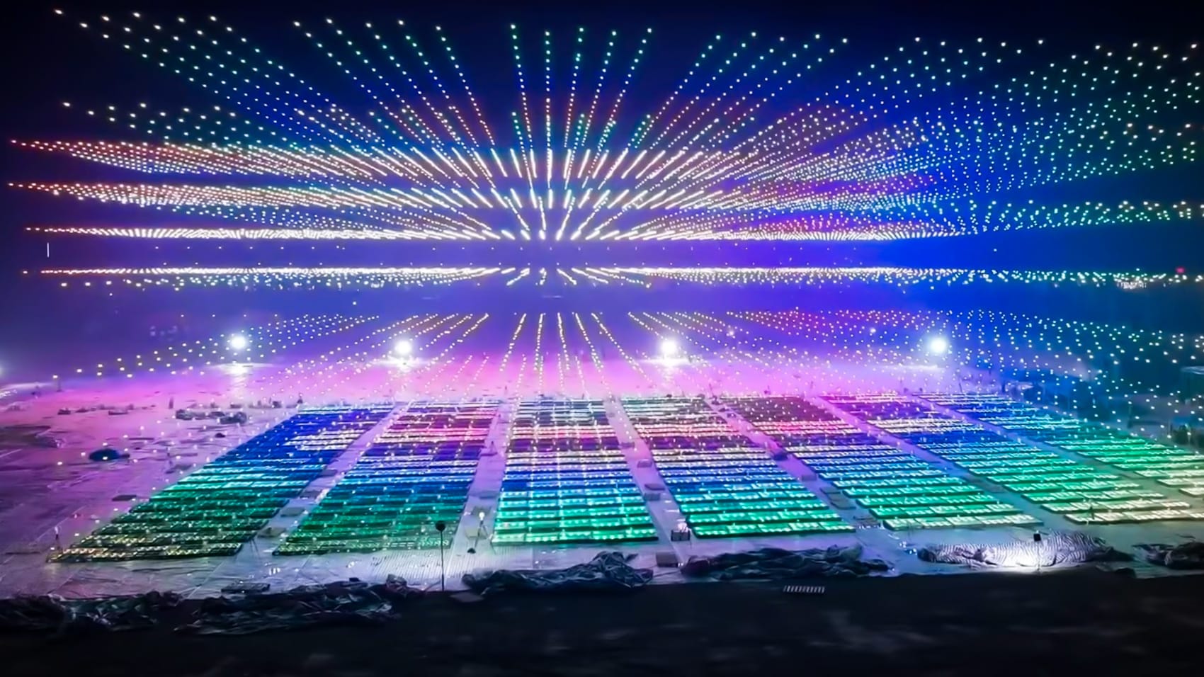 Thousands of light show drones forming a glowing burst pattern above a river.