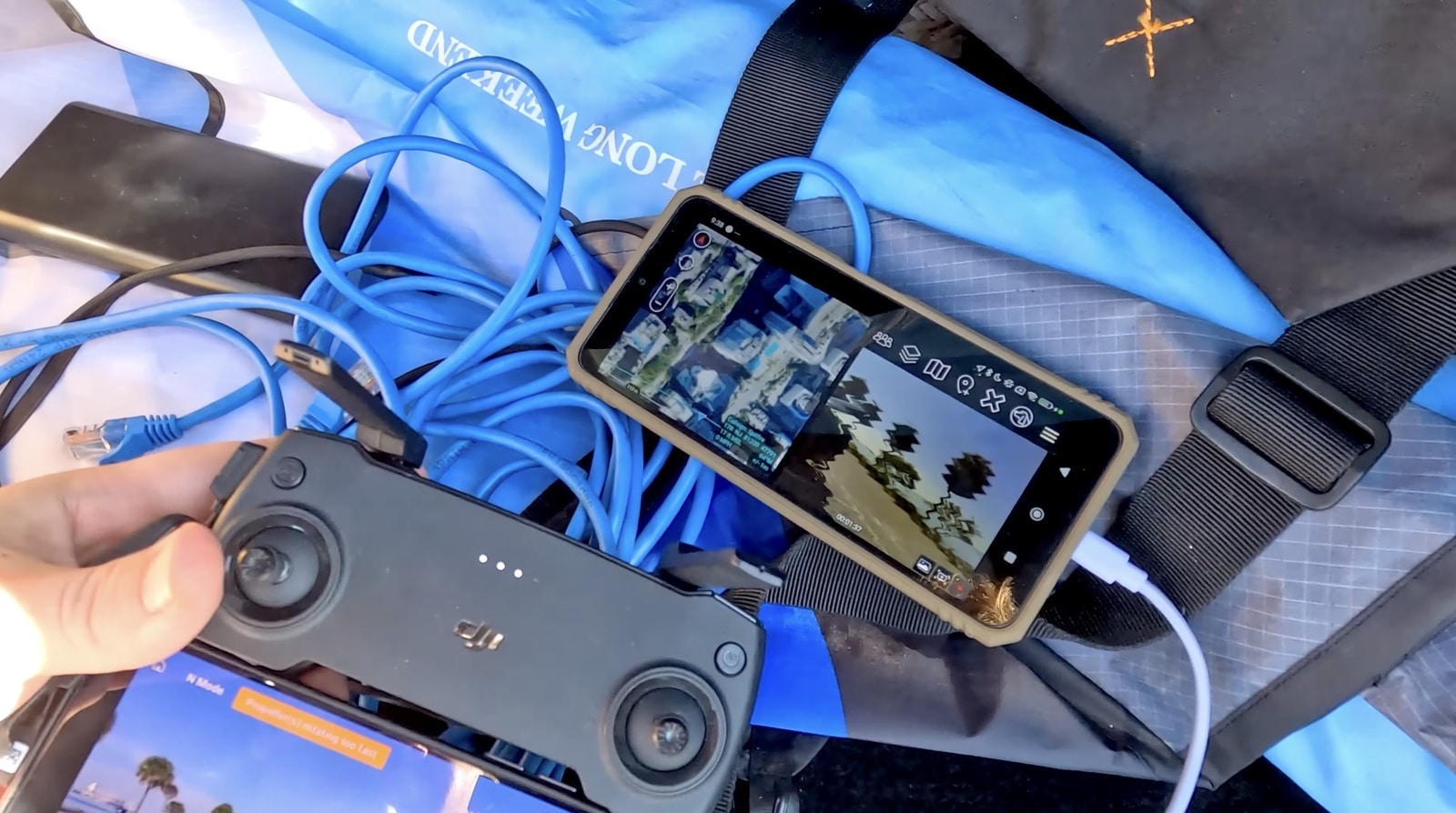 A hand holds a controller and phone running the mapping app atop a cable-filled bag.